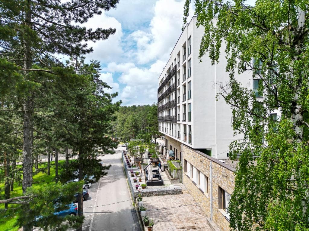 Modern white building next to pine forest and paved road under cloudy sky