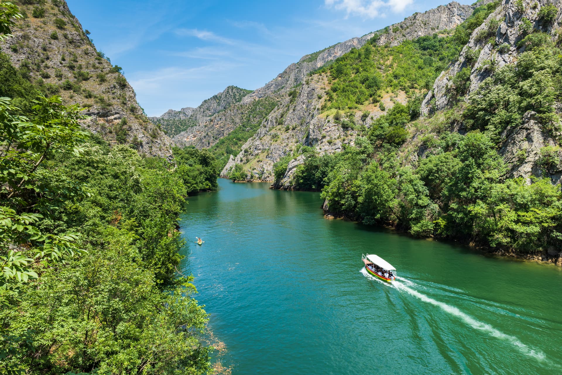 Tour boat cruising turquoise river through lush green canyon with steep rocky walls