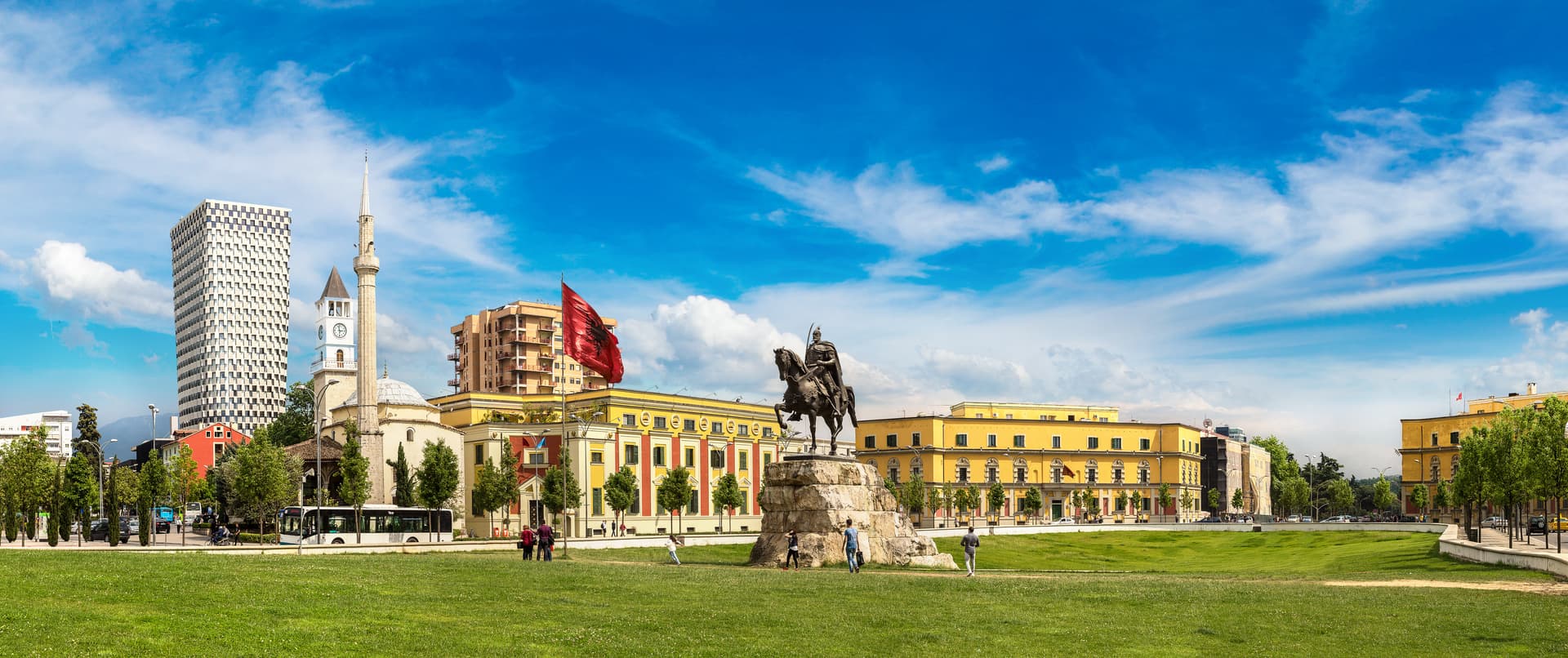 Equestrian statue in Skanderbeg Square, Tirana, with mosque and modern tower under blue sky.