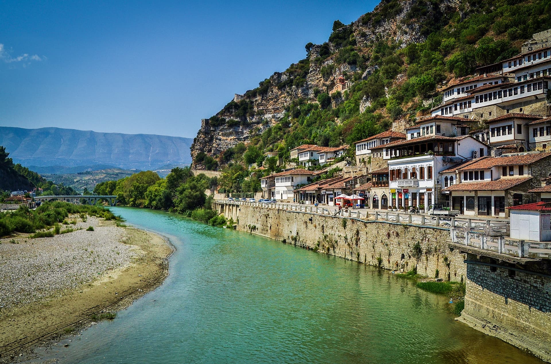 Historic white houses cascade down a steep hill above a turquoise river in Berat, Albania.