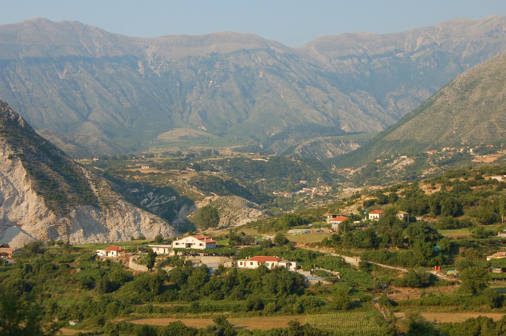 Village houses nestled in a lush green valley surrounded by large, arid mountains near Elbasan.