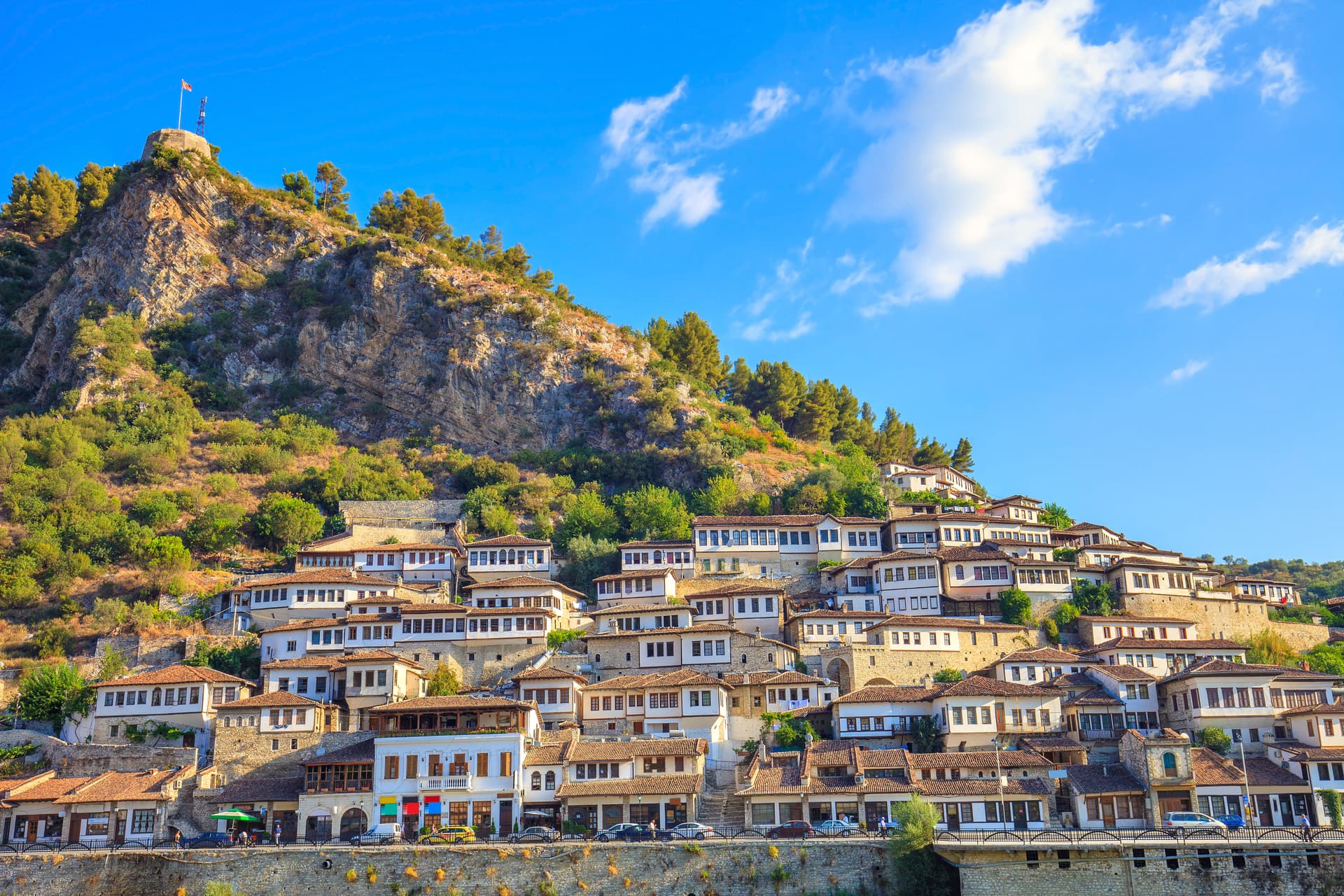White Ottoman-style houses climbing a steep hillside under a bright blue sky, Berat, Albania.