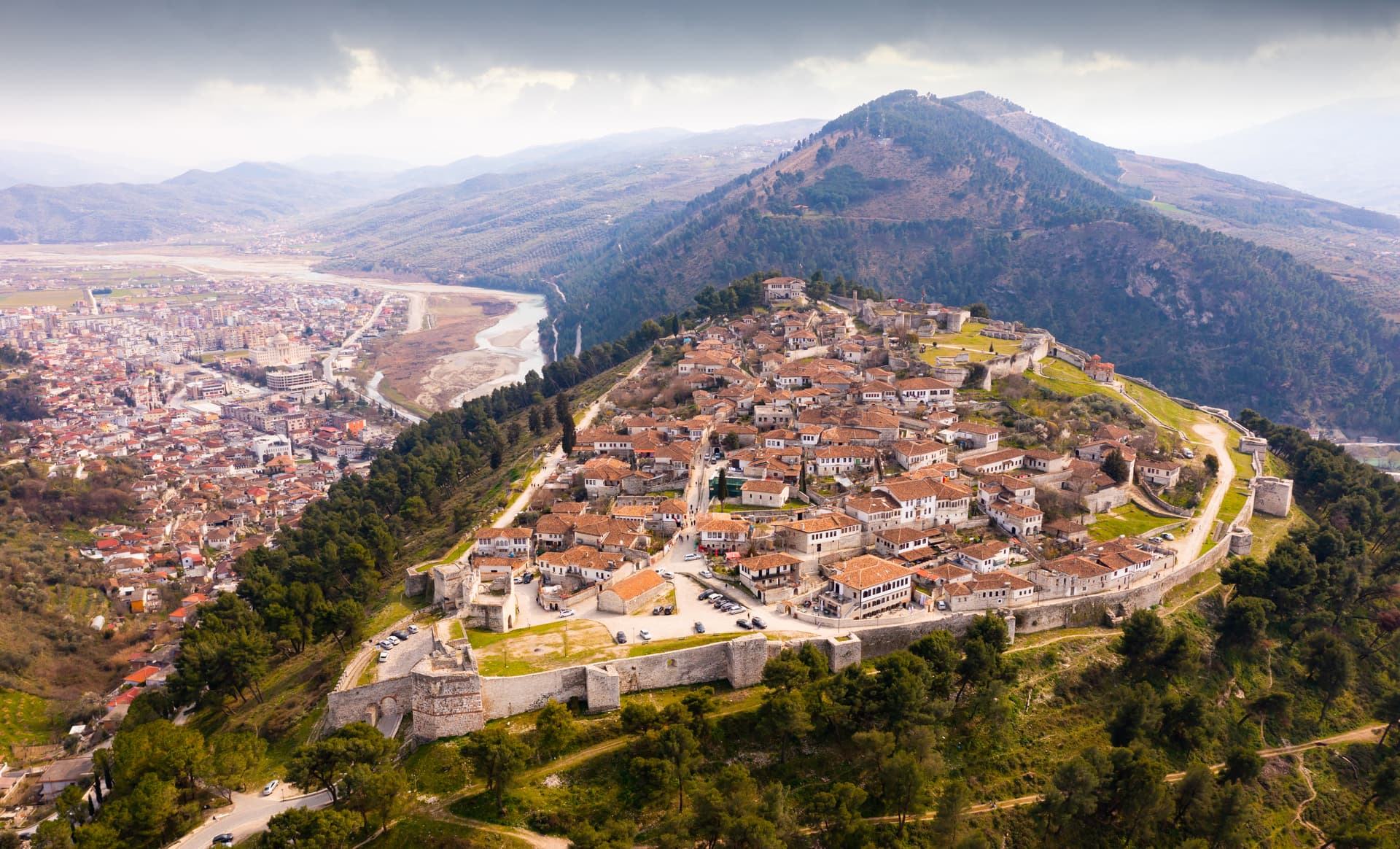 Aerial view of Berat Castle city overview with white houses and terracotta roofs nestled in mountains.