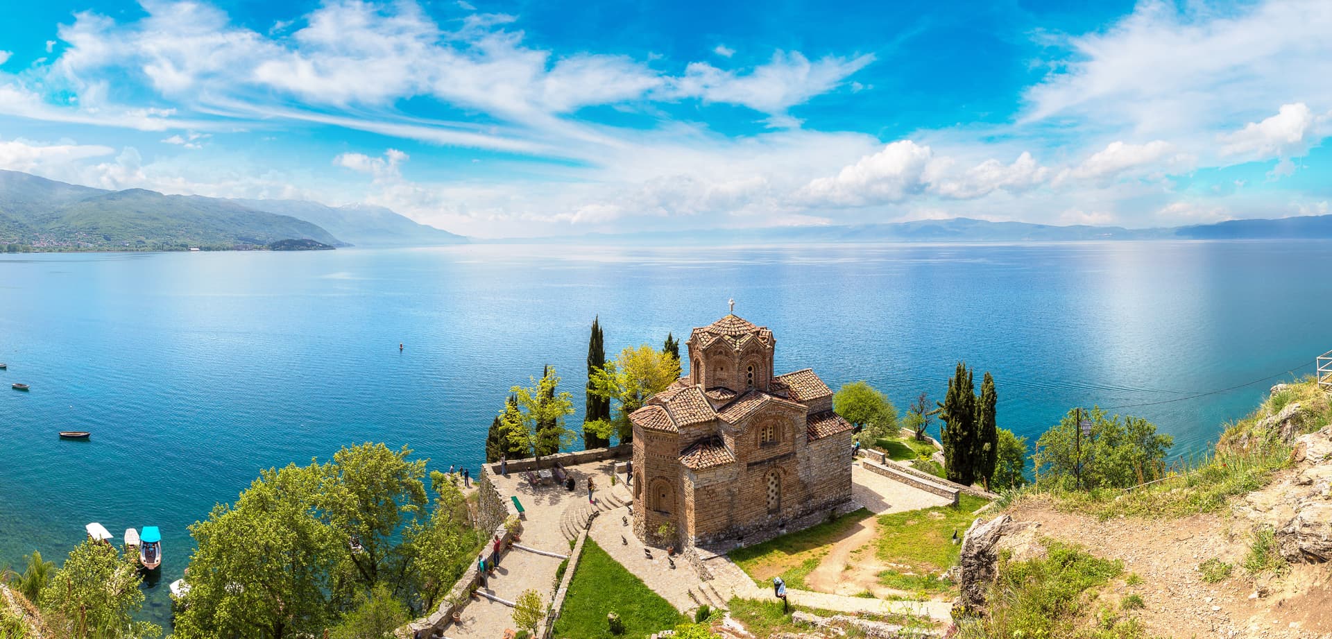 Church of St. John at Kaneo overlooking bright blue Lake Ohrid with mountains in distance.