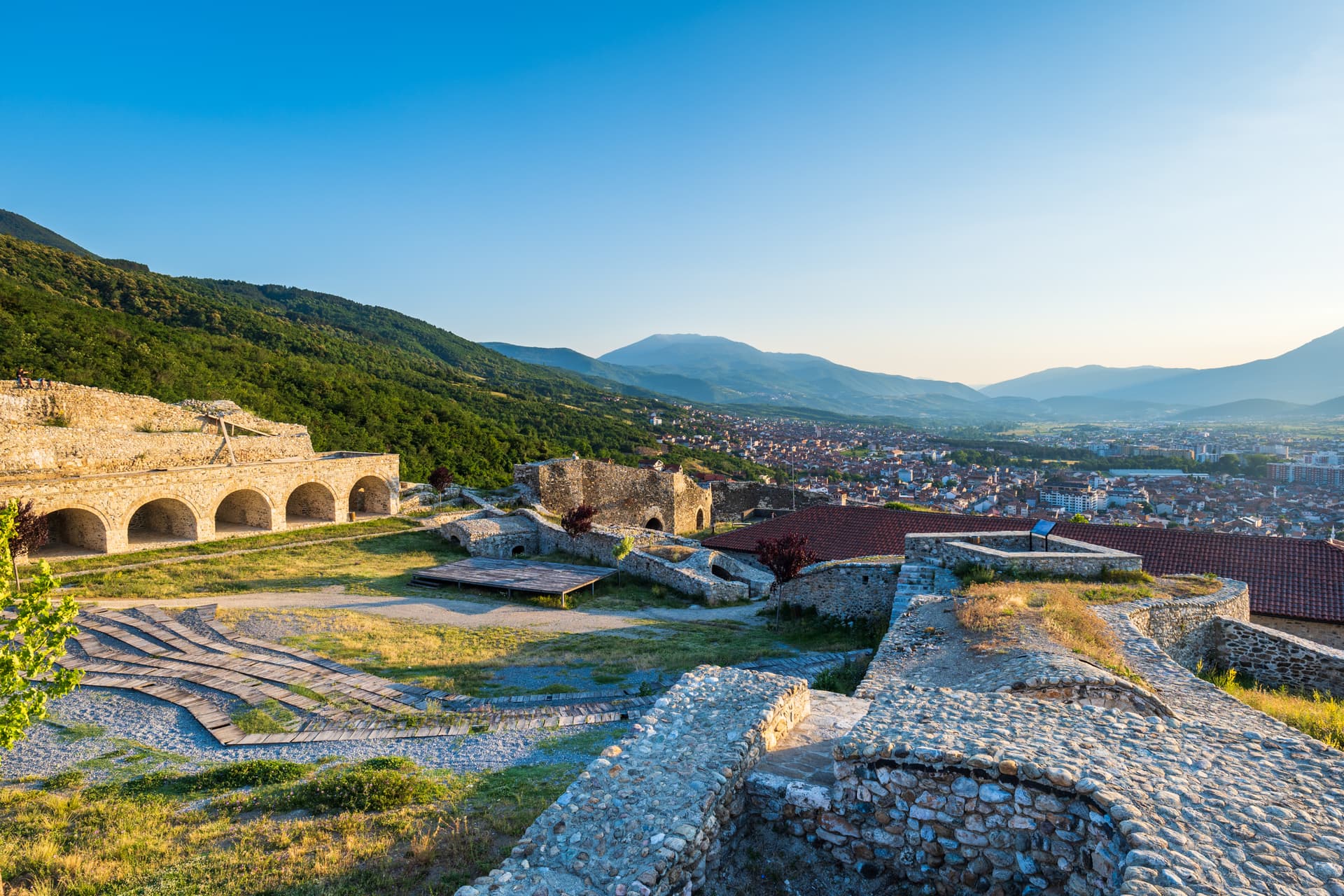 Stone ruins of Prizren Fortress overlooking the city and surrounding green mountains under a clear blue sky.