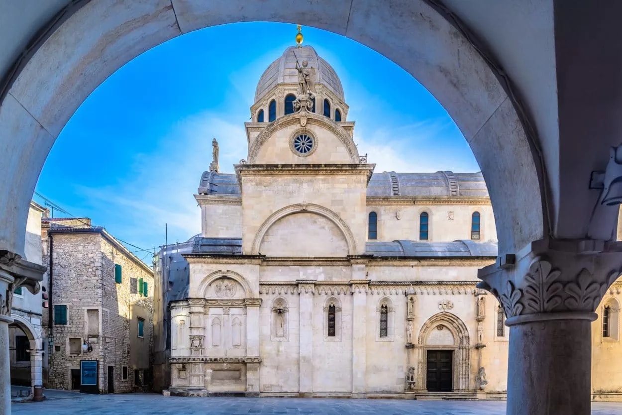 St. James Cathedral facade framed by stone arches in Šibenik, Croatia, under blue sky.