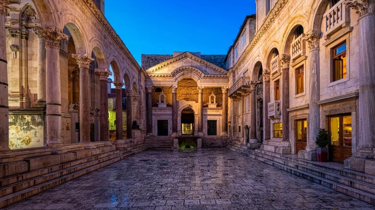 Stone courtyard with Romanesque arches and columns illuminated at twilight in Split.