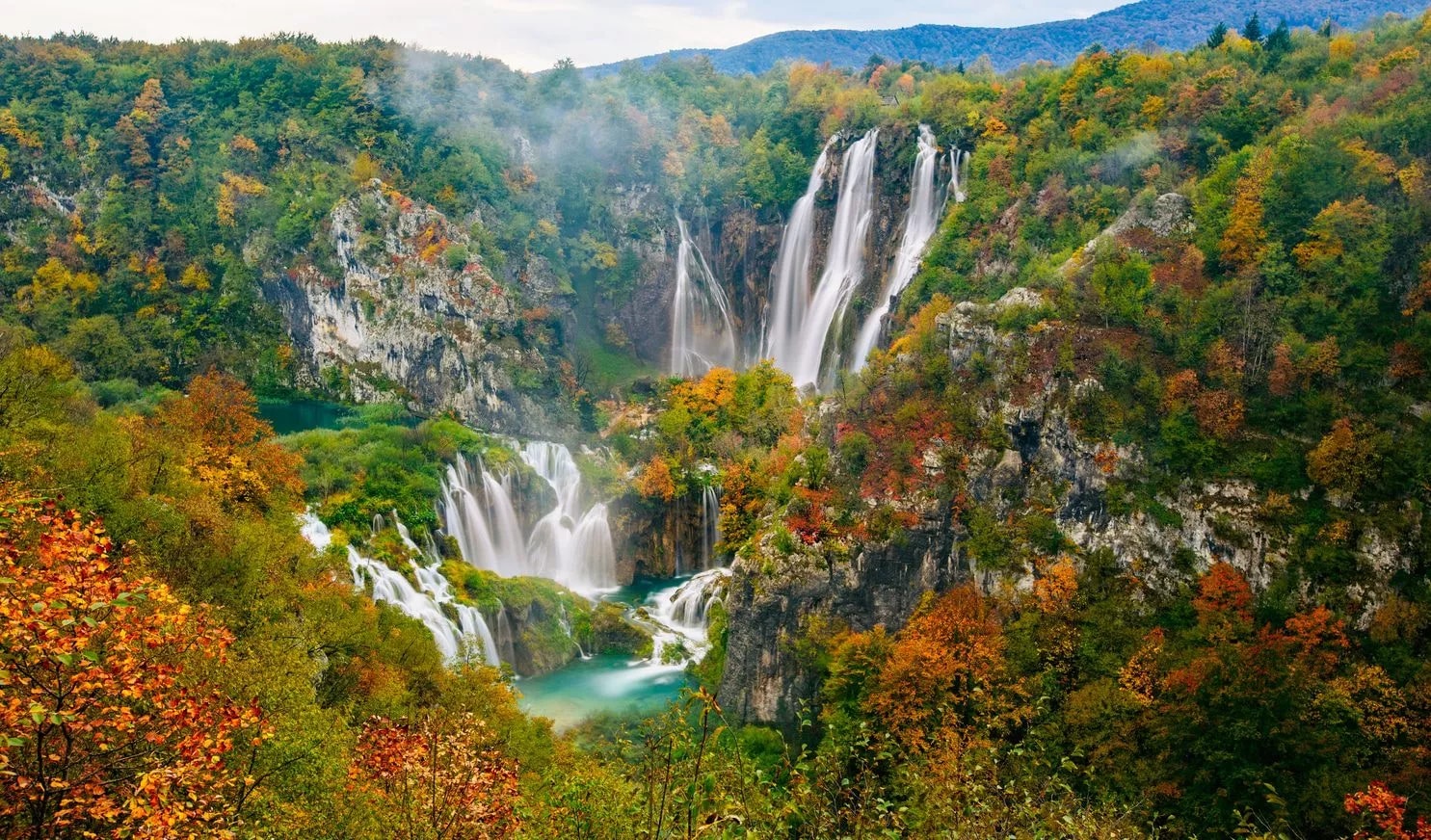 Large waterfalls cascading down cliffs surrounded by autumn foliage in Plitvice National Park.