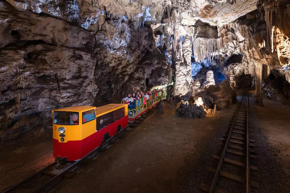 Postojna Cave train full of visitors riding through cavern with stalactites and stalagmites.
