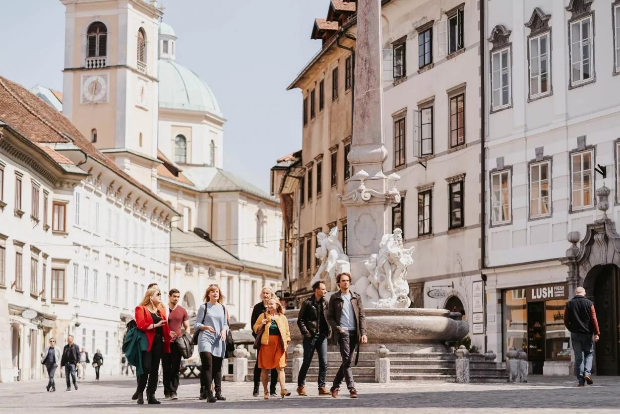 Tourists walking near fountain and church tower in old town Ljubljana.