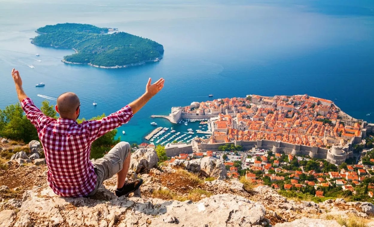 Man celebrating view of Dubrovnik old town walls and Adriatic Sea from Mount Srd.