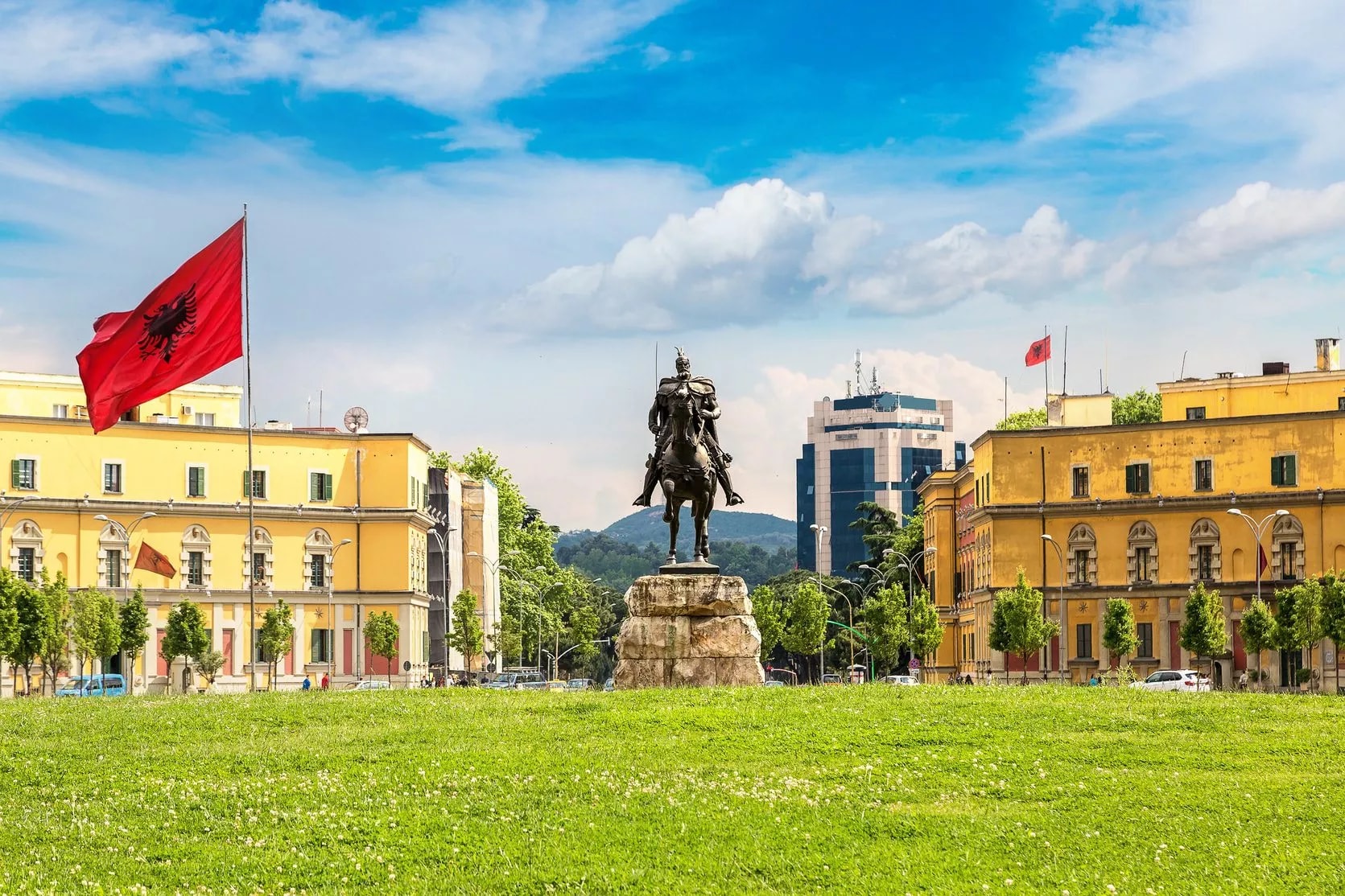 Skanderbeg Monument on horseback in grassy square with Albanian flag in Tirana.