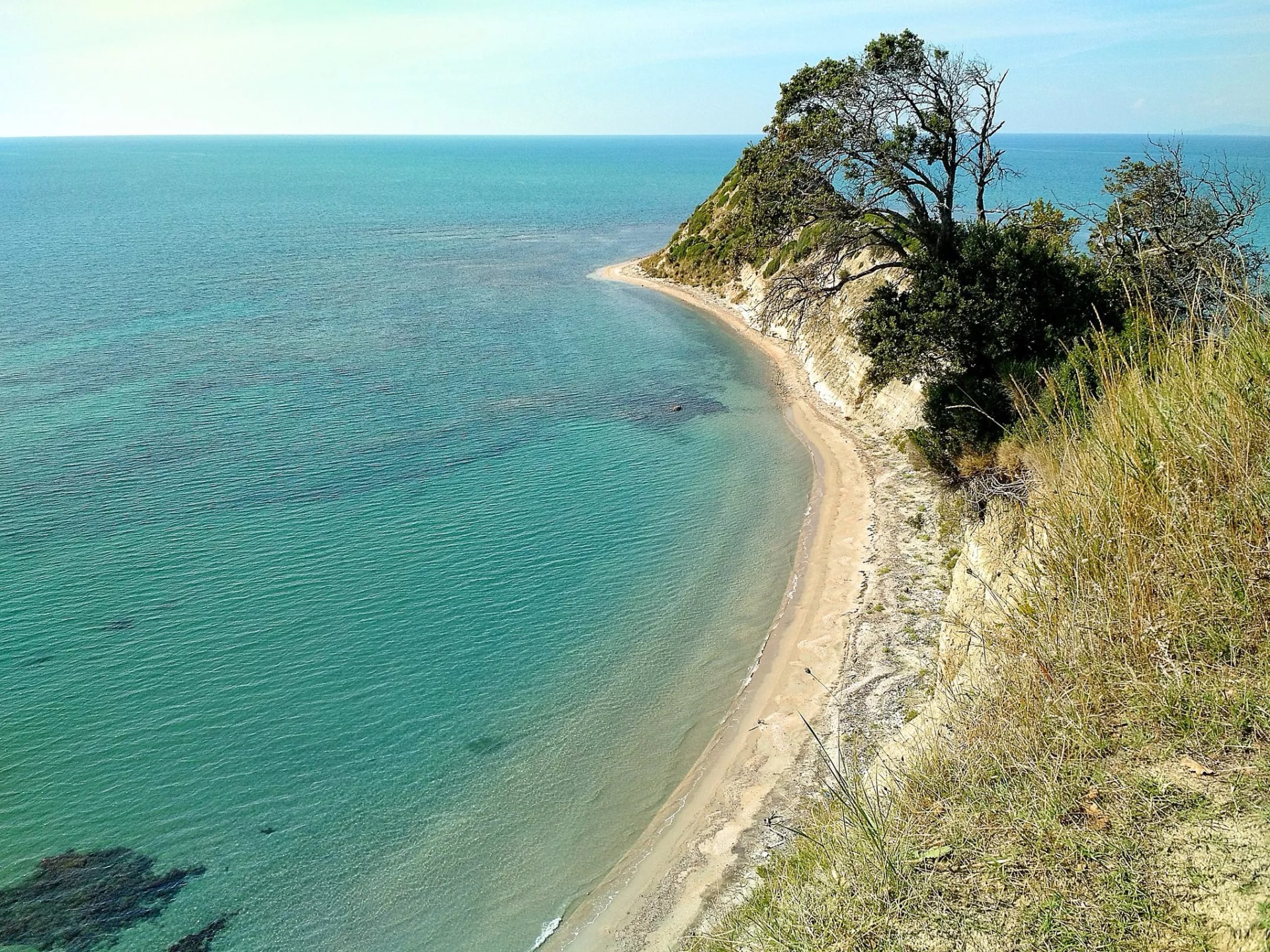 Sandy cove below a vegetated cliff overlooking turquoise sea at Durres Cape of Rodon.