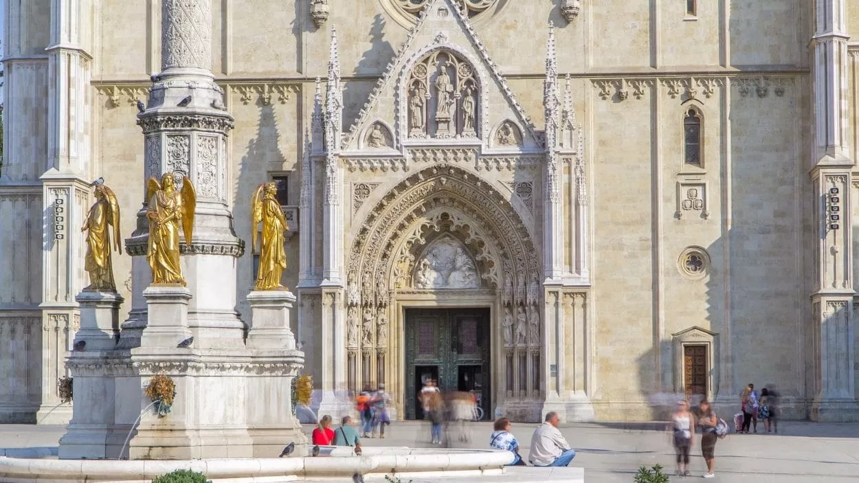 Zagreb Cathedral facade with golden angel statues and people sitting near a fountain.