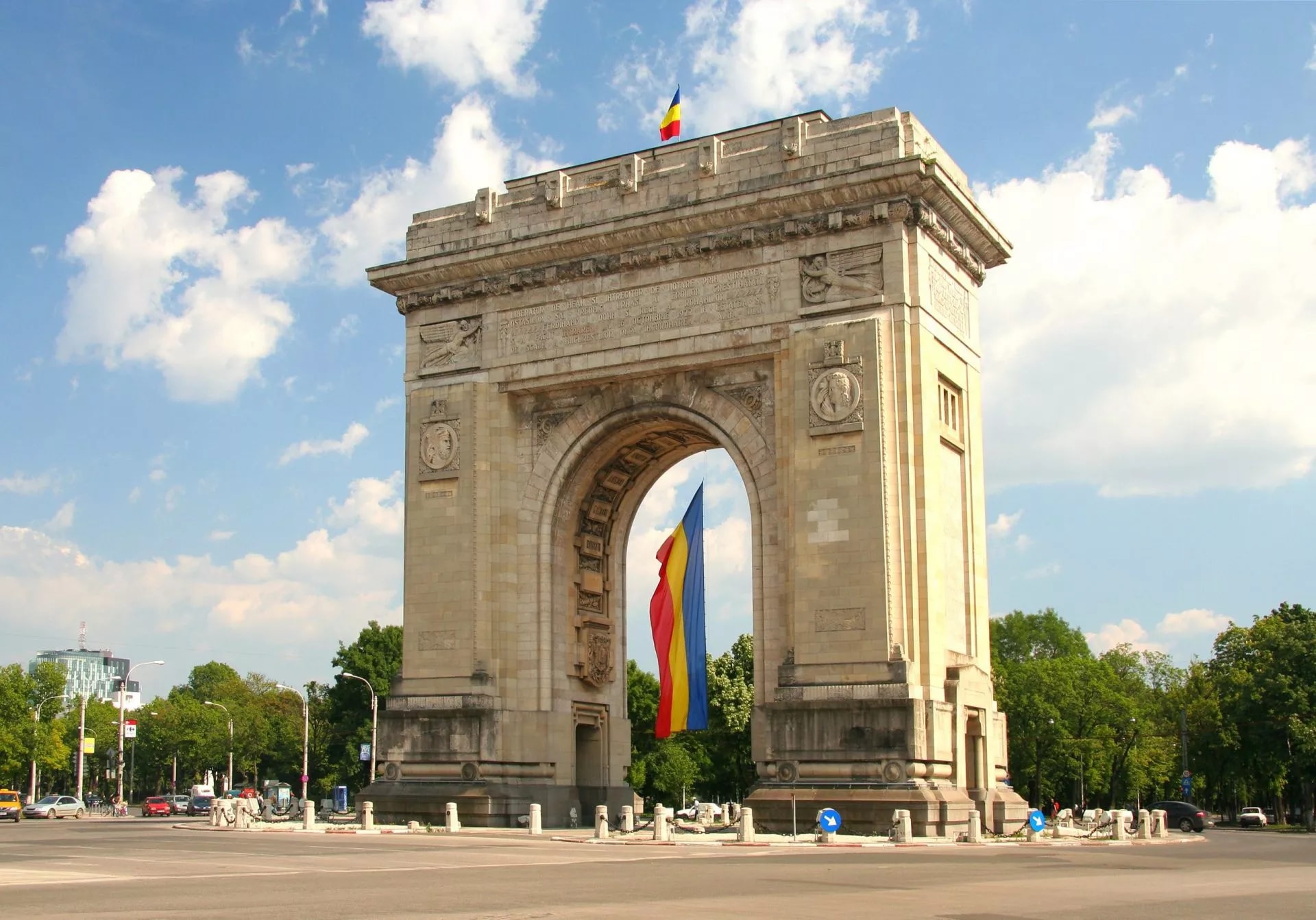 Triumphal Arch with Romanian flag hanging through the archway under a blue sky.