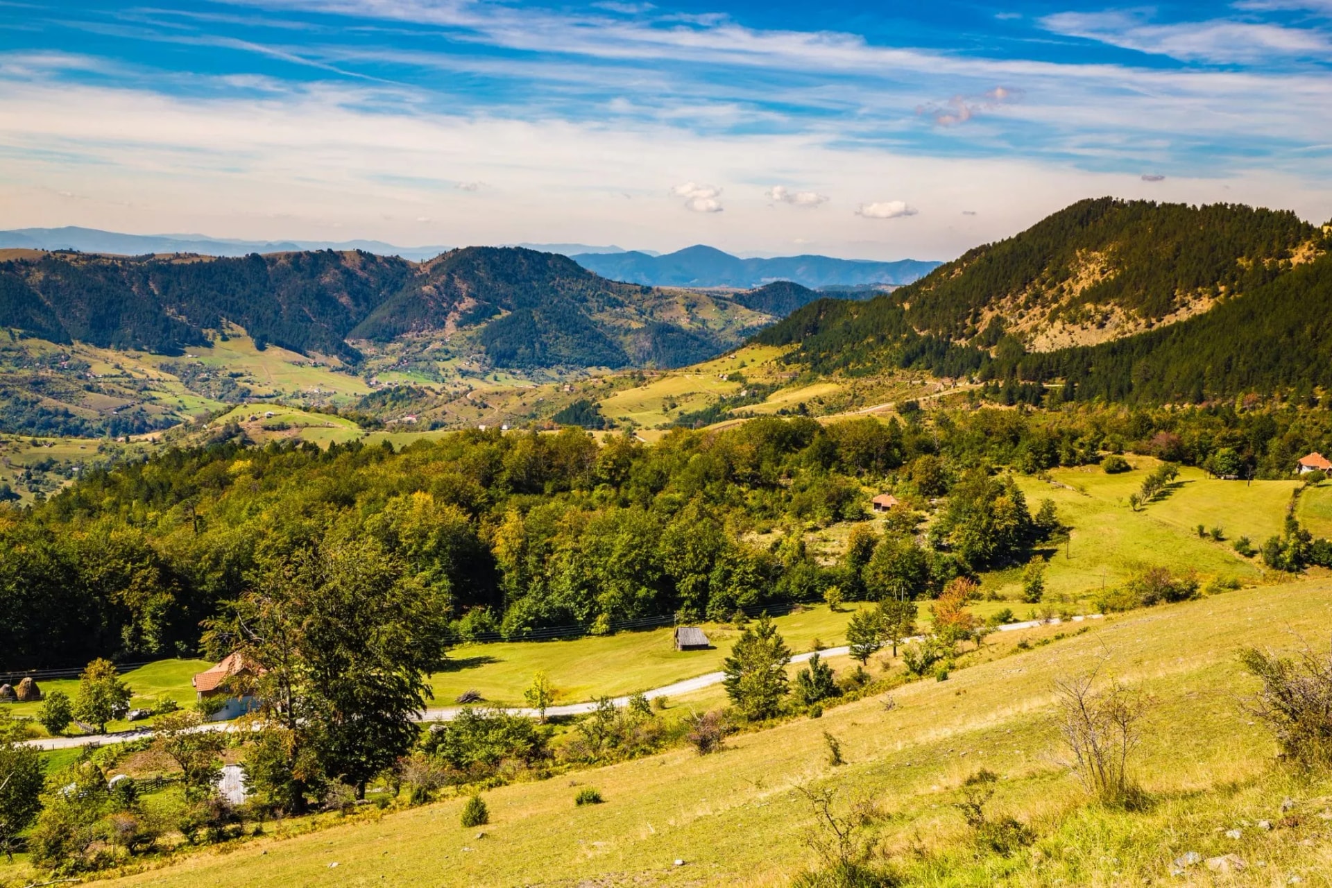 Mountain panorama of Zlatibor with rolling green hills, forests, and scattered houses under a blue sky.