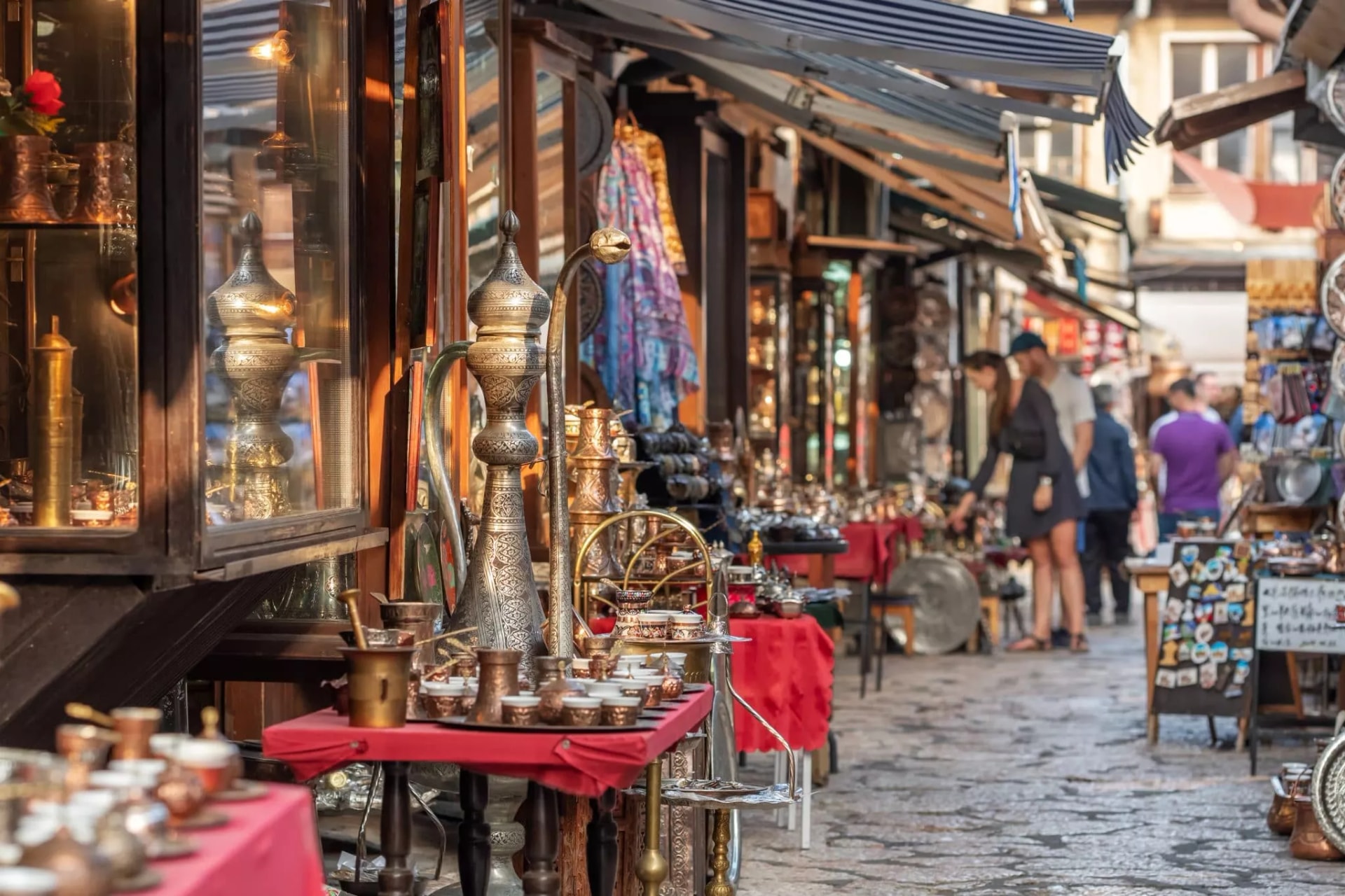 Sarajevo street market stalls displaying ornate metalwork and coffee sets on cobblestones.