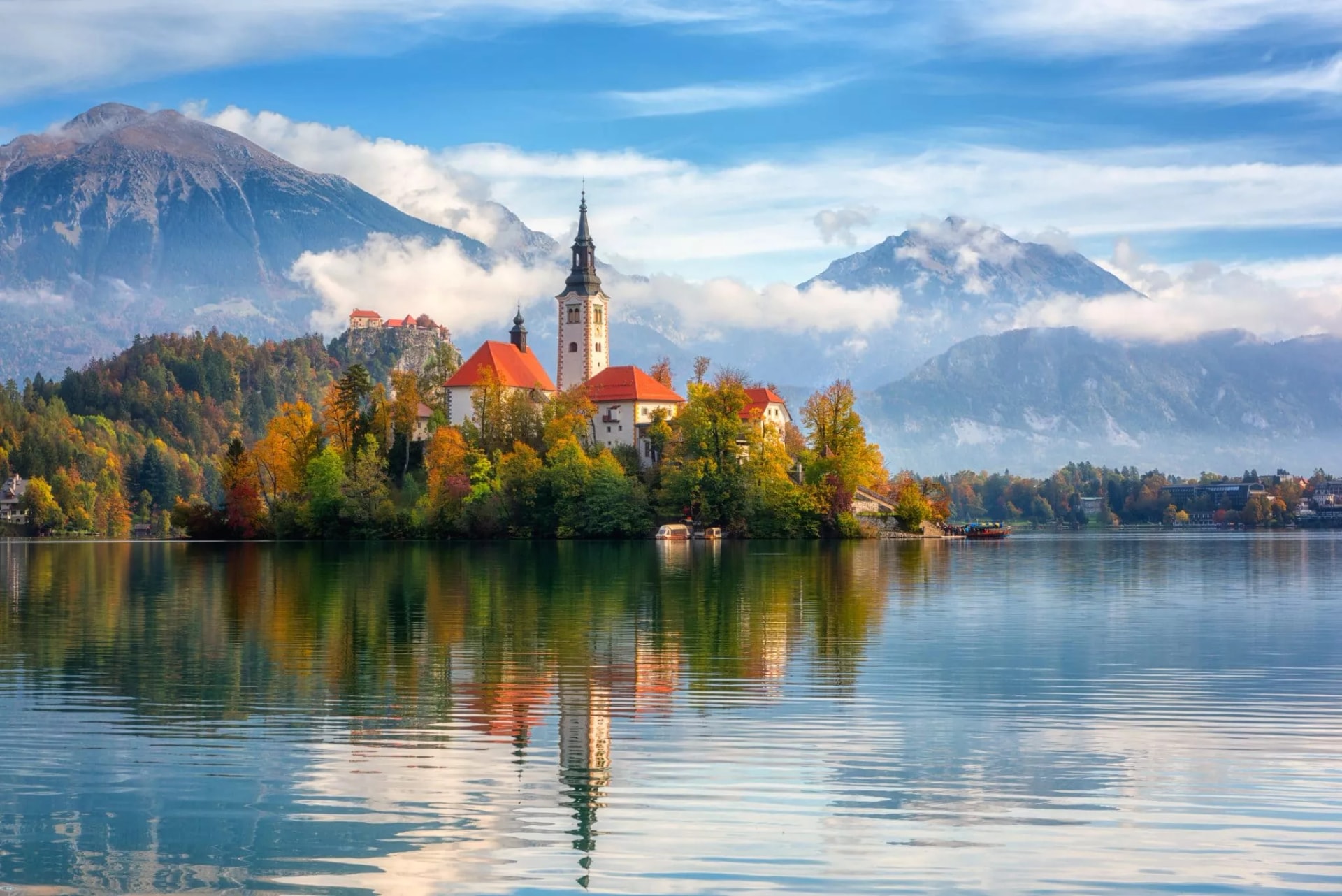 Church on island in Lake Bled with autumn trees and Julian Alps in background