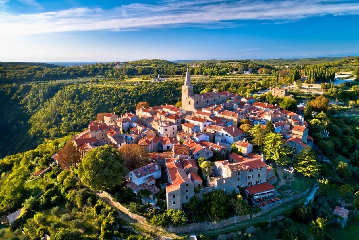 Hilltop town of Grožnjan with terracotta roofs and a prominent church tower surrounded by green forest.