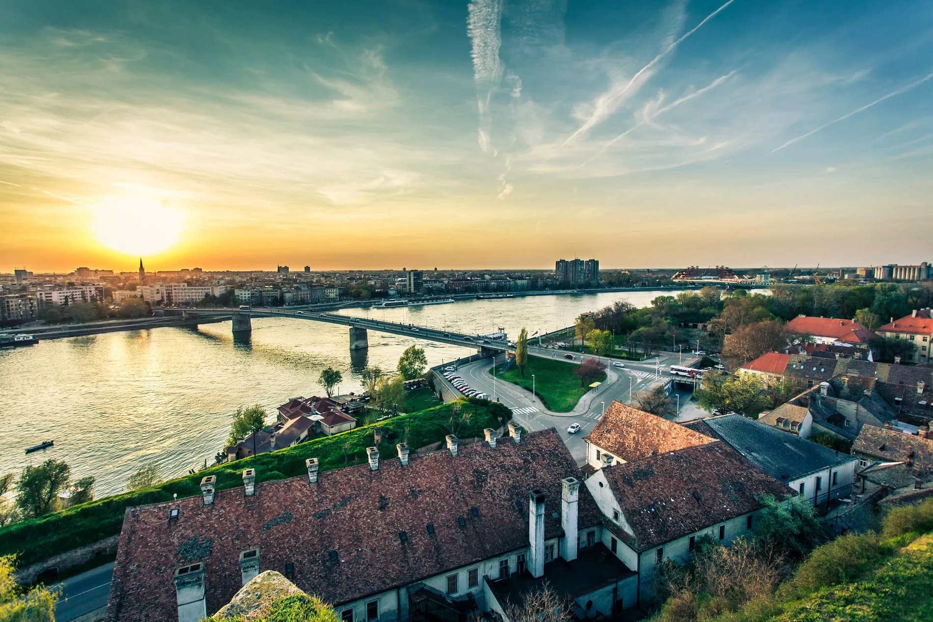 Novi Sad river panorama at sunset with bridge, city skyline, and terracotta rooftops.