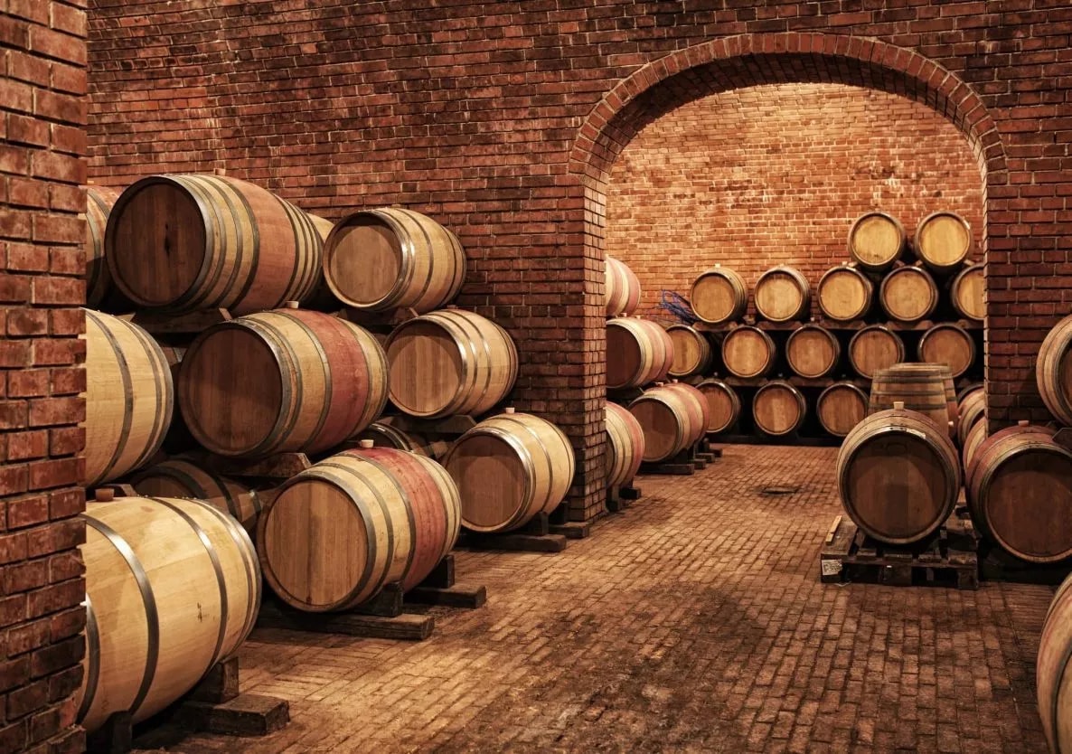Wooden wine barrels stacked in a traditional brick cellar through an arched doorway