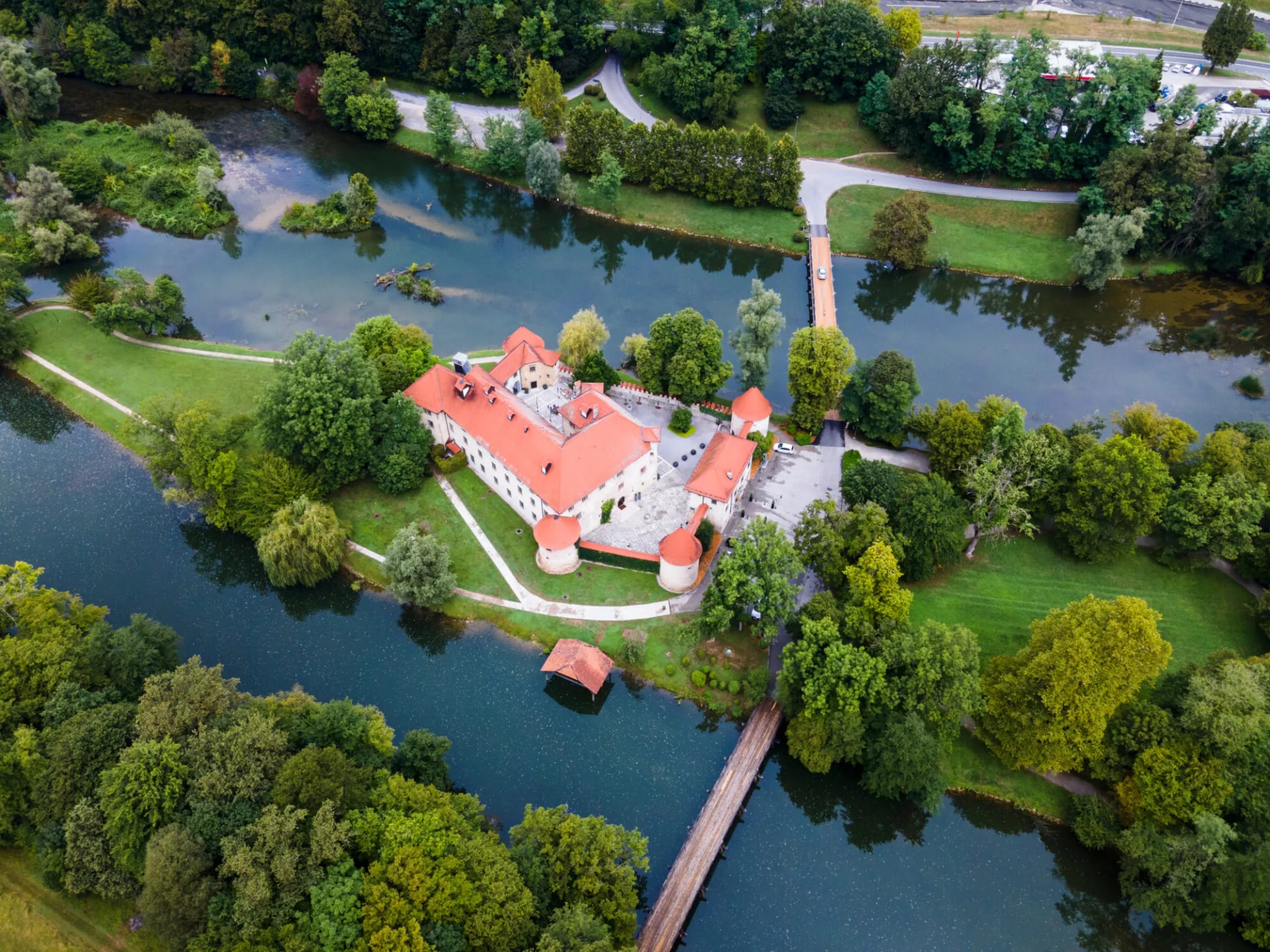 Aerial view of Otočec Castle surrounded by a river, lush green trees, and bridges.
