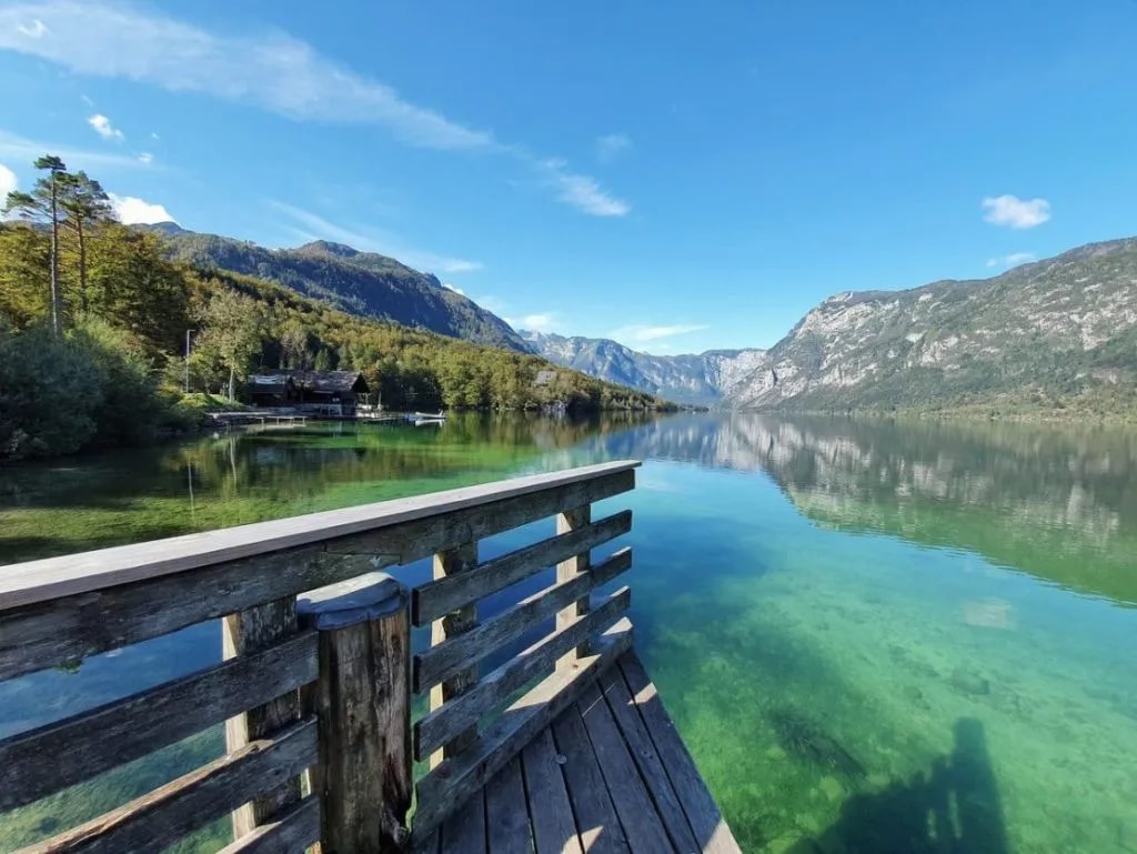 Wooden dock overlooking clear turquoise water of Bohinj Lake with mountains and forest