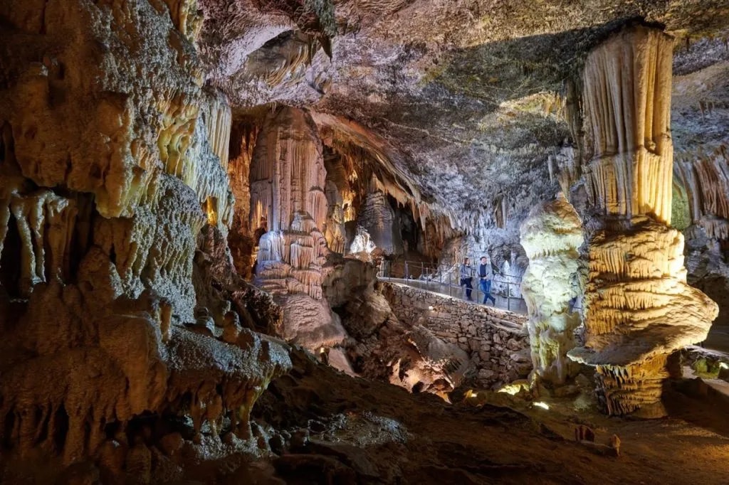 Tourists viewing massive illuminated stalactites and stalagmites inside Postojna Cave.