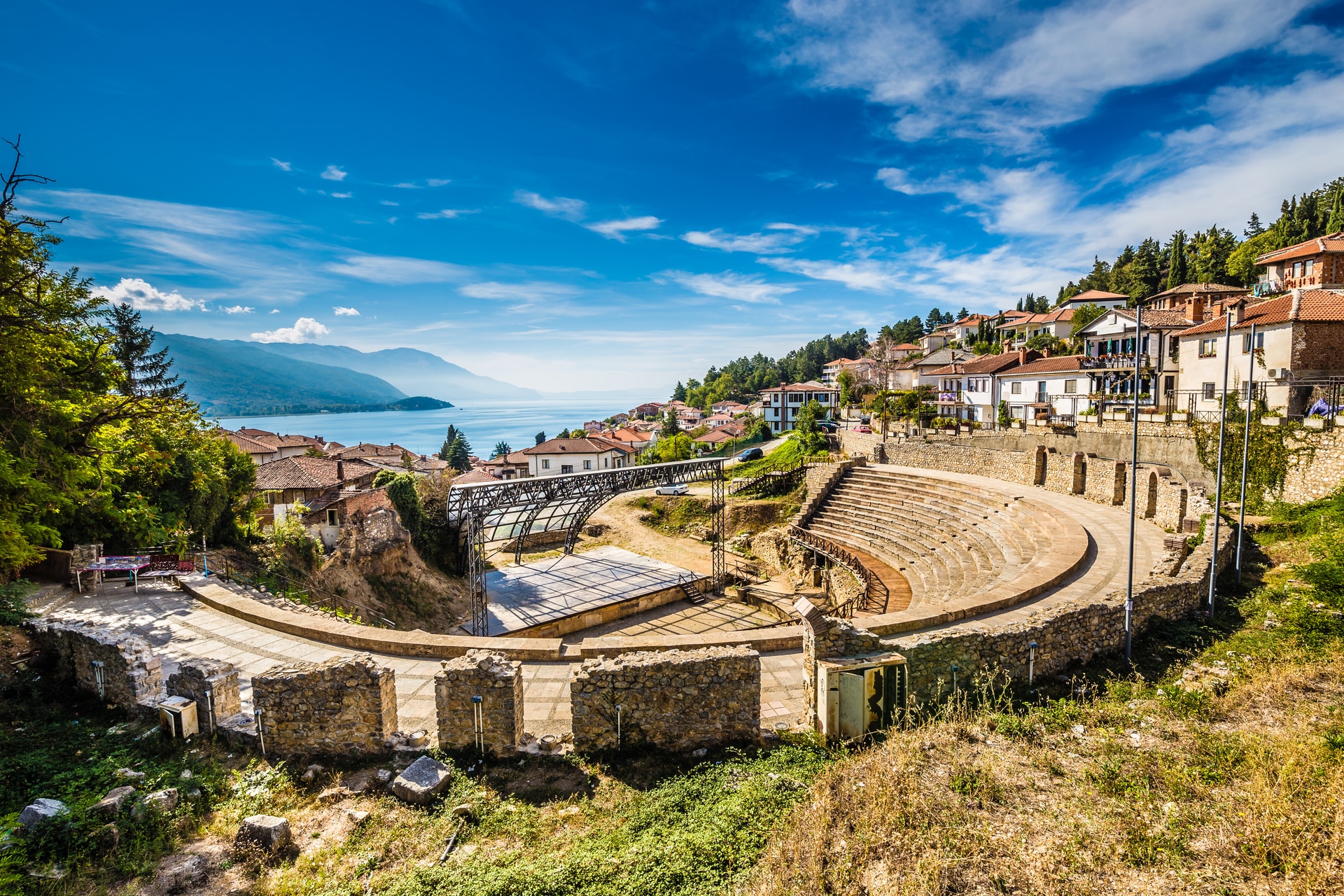 Ancient Roman theatre ruins overlooking Ohrid town and lake under a bright blue sky.