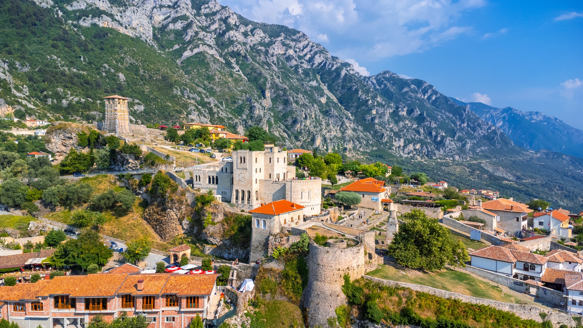 Kruje Castle complex with stone walls nestled against steep, green mountains under a blue sky in Albania.
