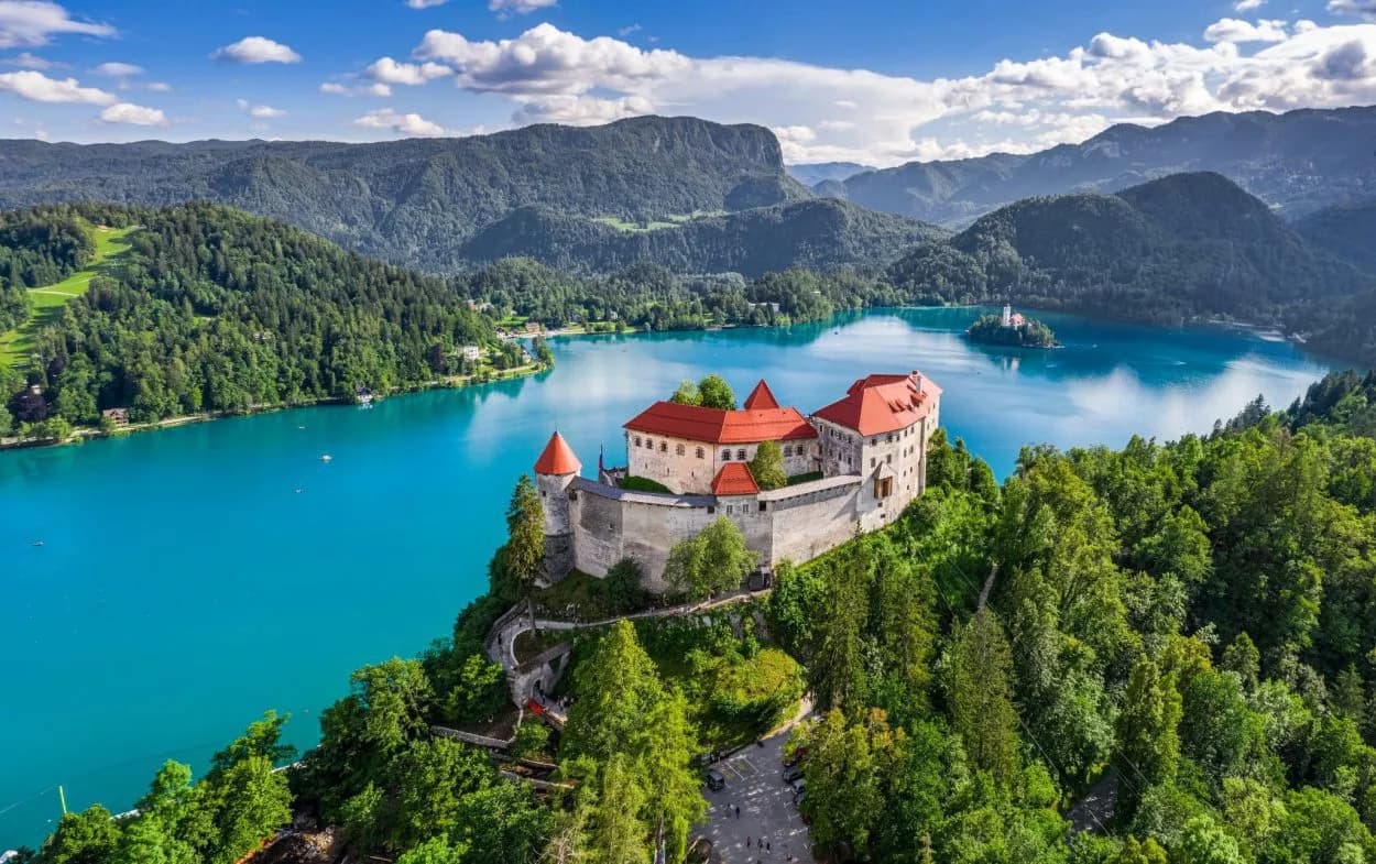 Bled Castle overlooking turquoise Lake Bled with island church and forested mountains, Slovenia.