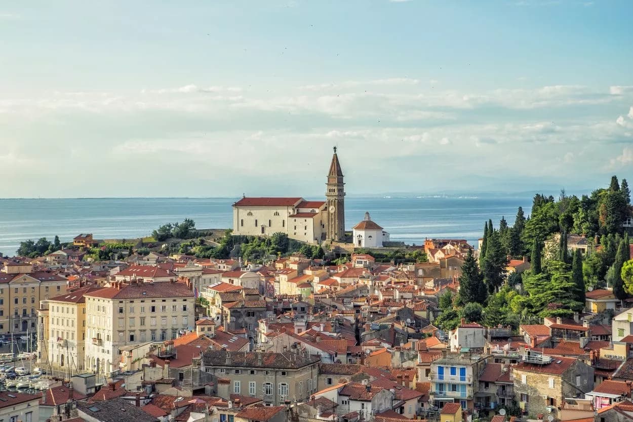 Town of Piran coastal view with dense terracotta roofs and a prominent church tower overlooking the sea.