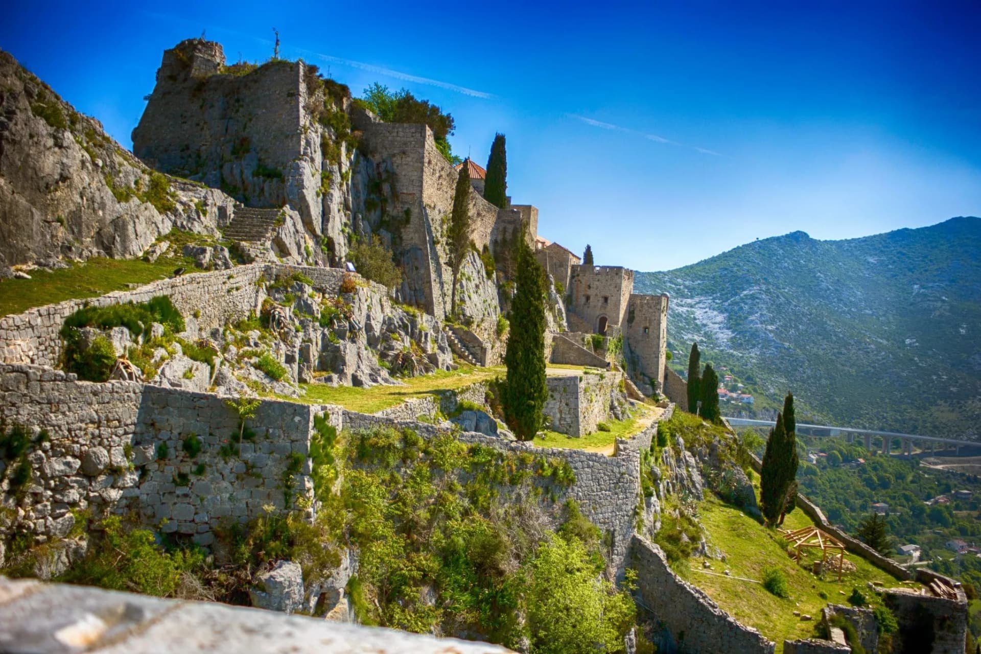 Klis Fortress ruins on a rocky hillside above Split under a bright blue sky.