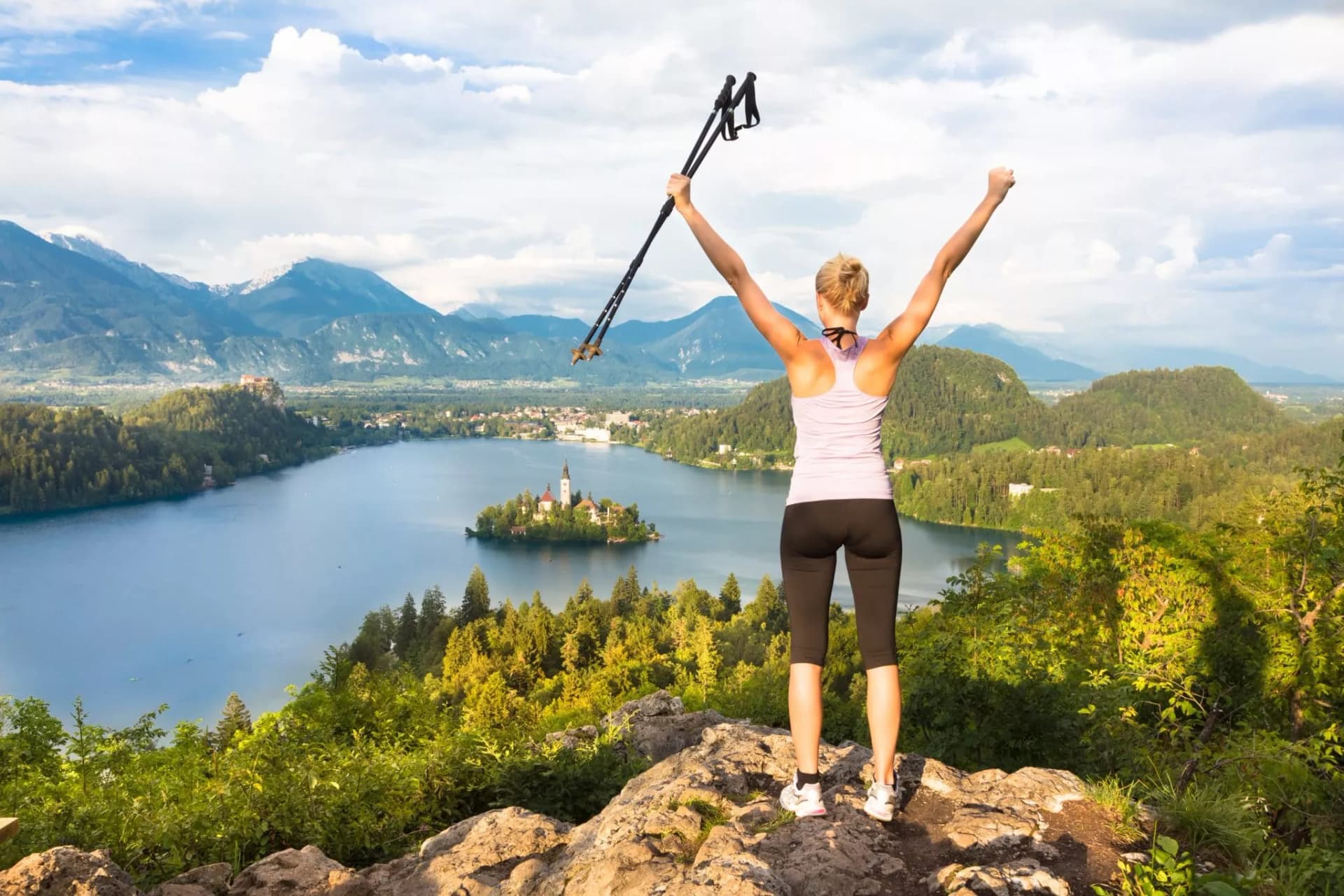Hiker with poles celebrating overlooking Lake Bled island and Julian Alps, Slovenia