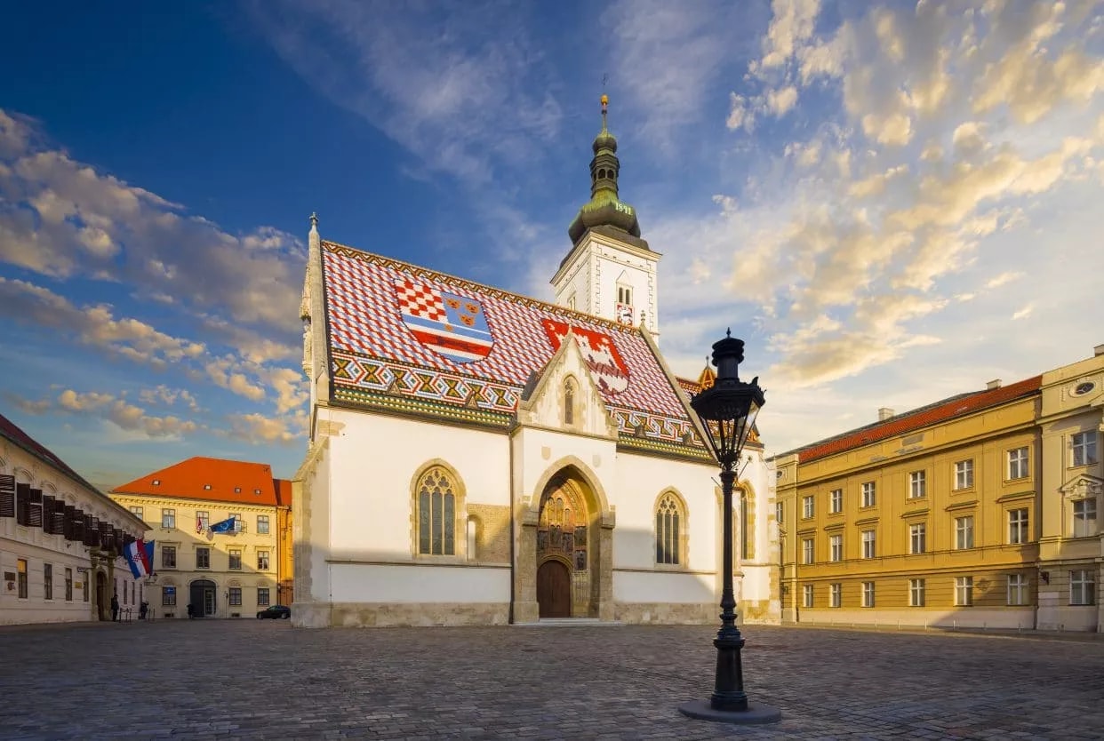 Church of St. Mark with colorful tiled roof in Zagreb square under blue sky.