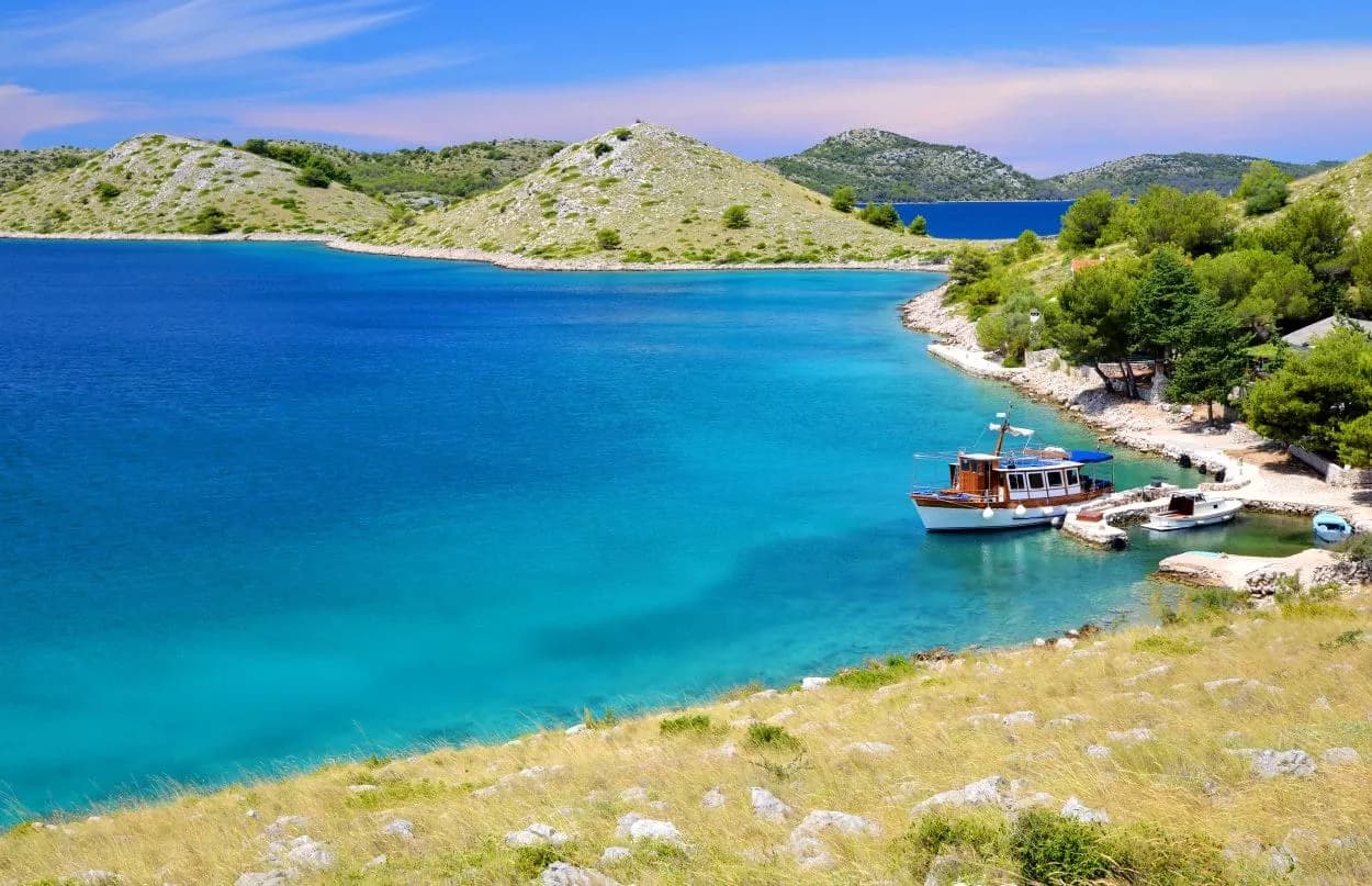 Boat docked in turquoise cove with arid hillsides, Kornati Islands.