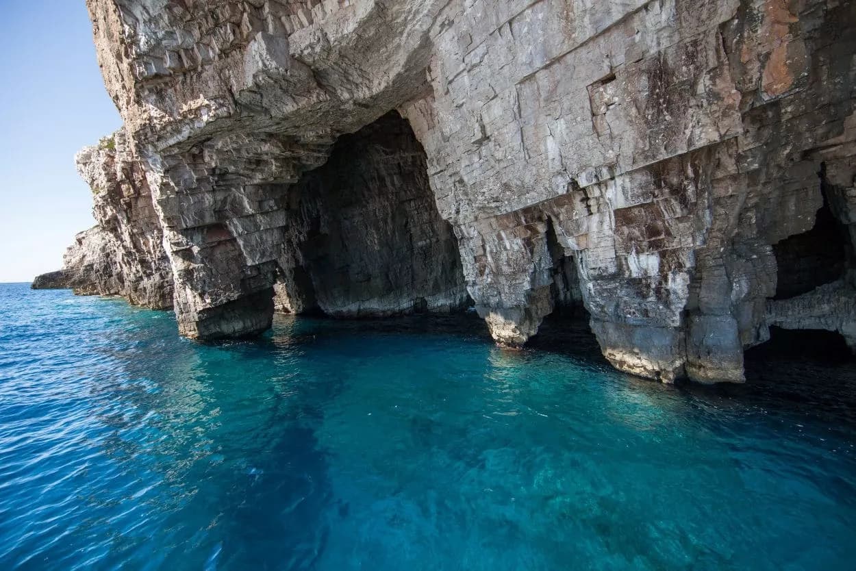 Boat approaching sea caves in steep rocky cliffs with vibrant blue water.