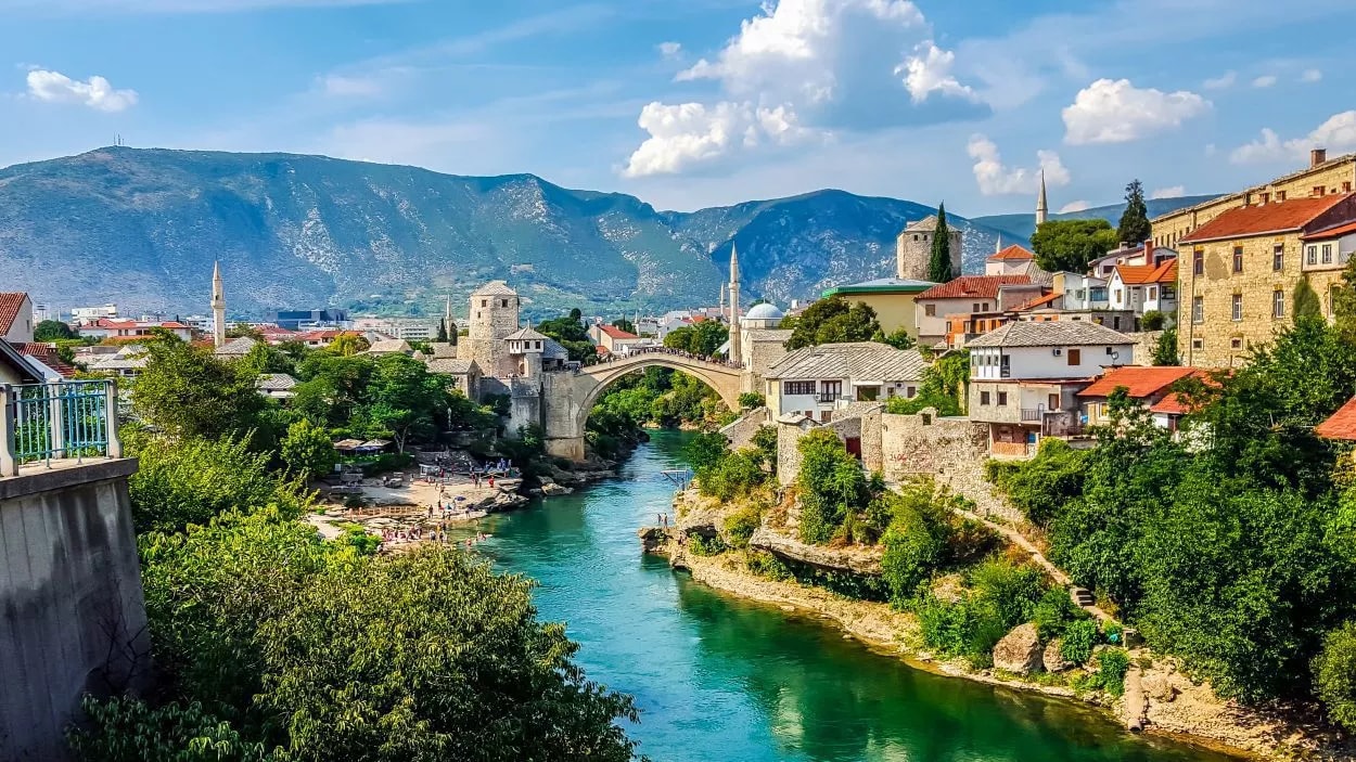 Stari Most bridge over turquoise river in Mostar with historic buildings and mountains.