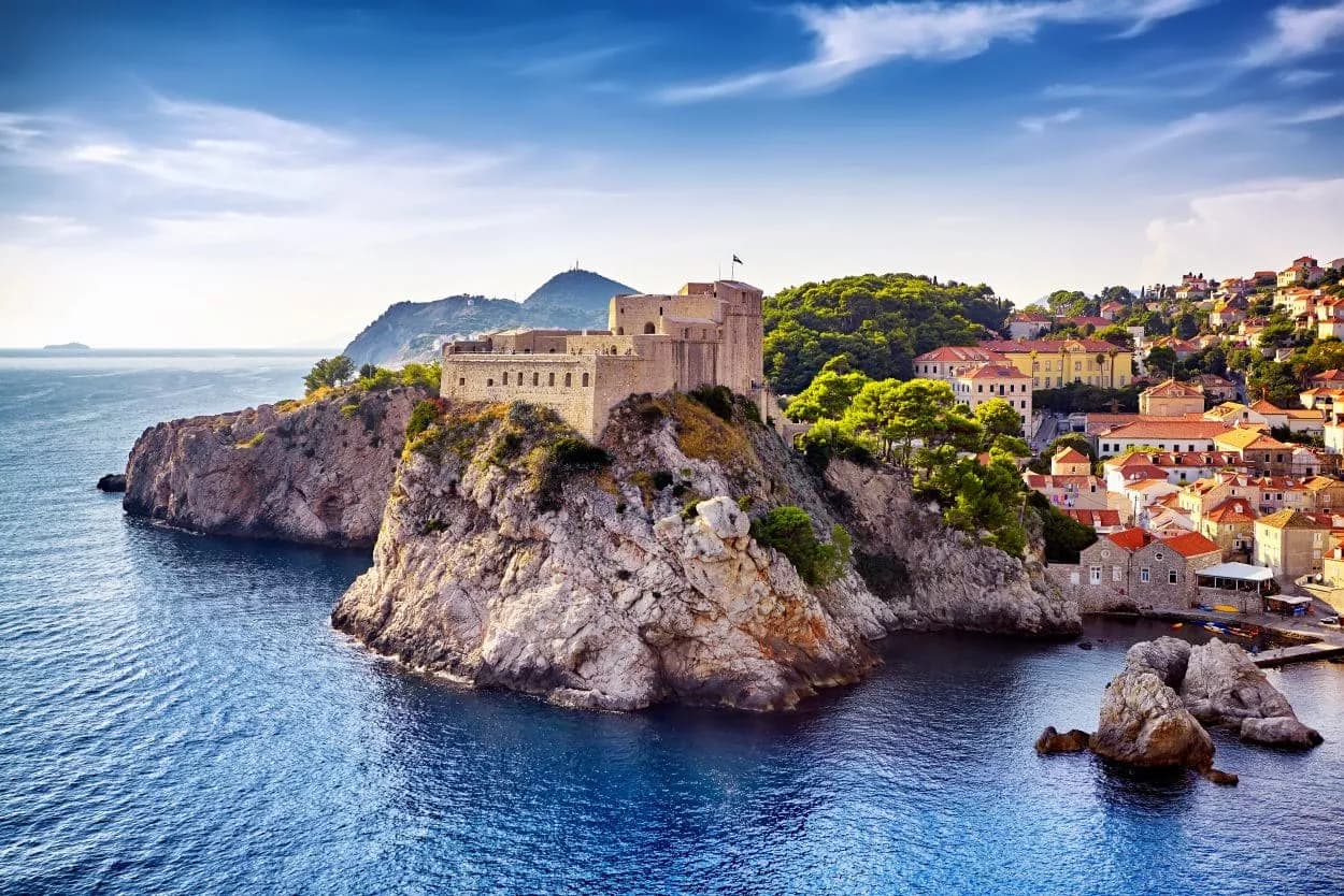 Stone fortress atop rocky cliffs overlooking blue sea water near Dubrovnik city.