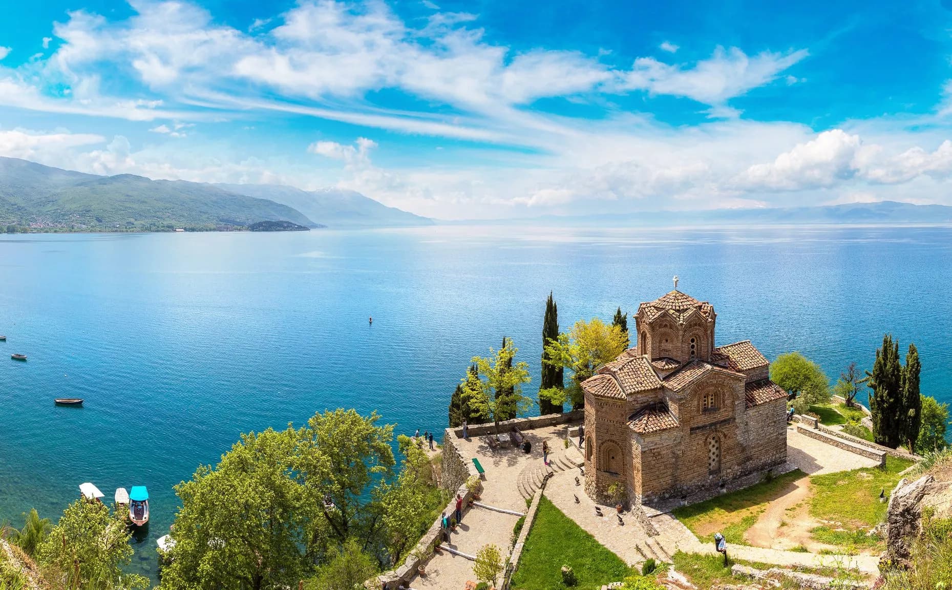 Church of St. John at Kaneo overlooking Lake Ohrid and surrounding mountains under blue sky.