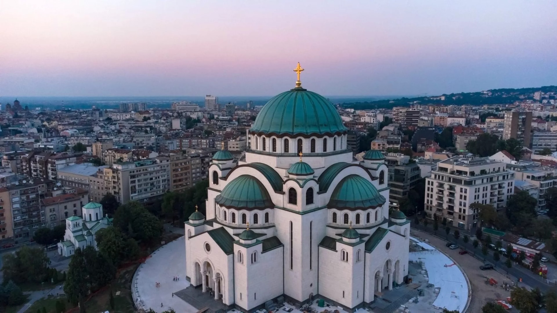 Saint Sava Church with green domes in Belgrade cityscape at dusk.