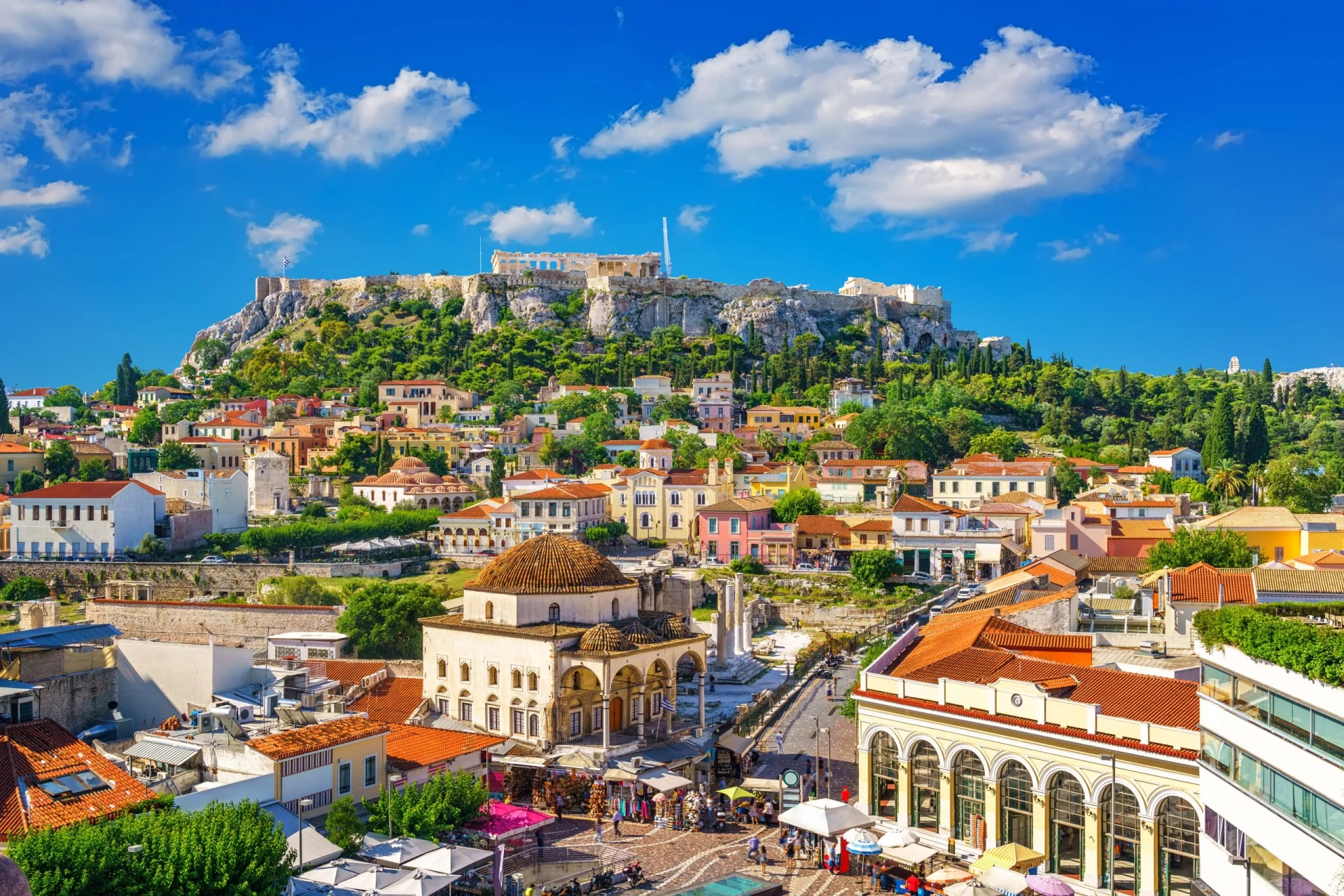 View of the Acropolis from the Plaka district in Athens, Greece, with colorful buildings and blue sky.
