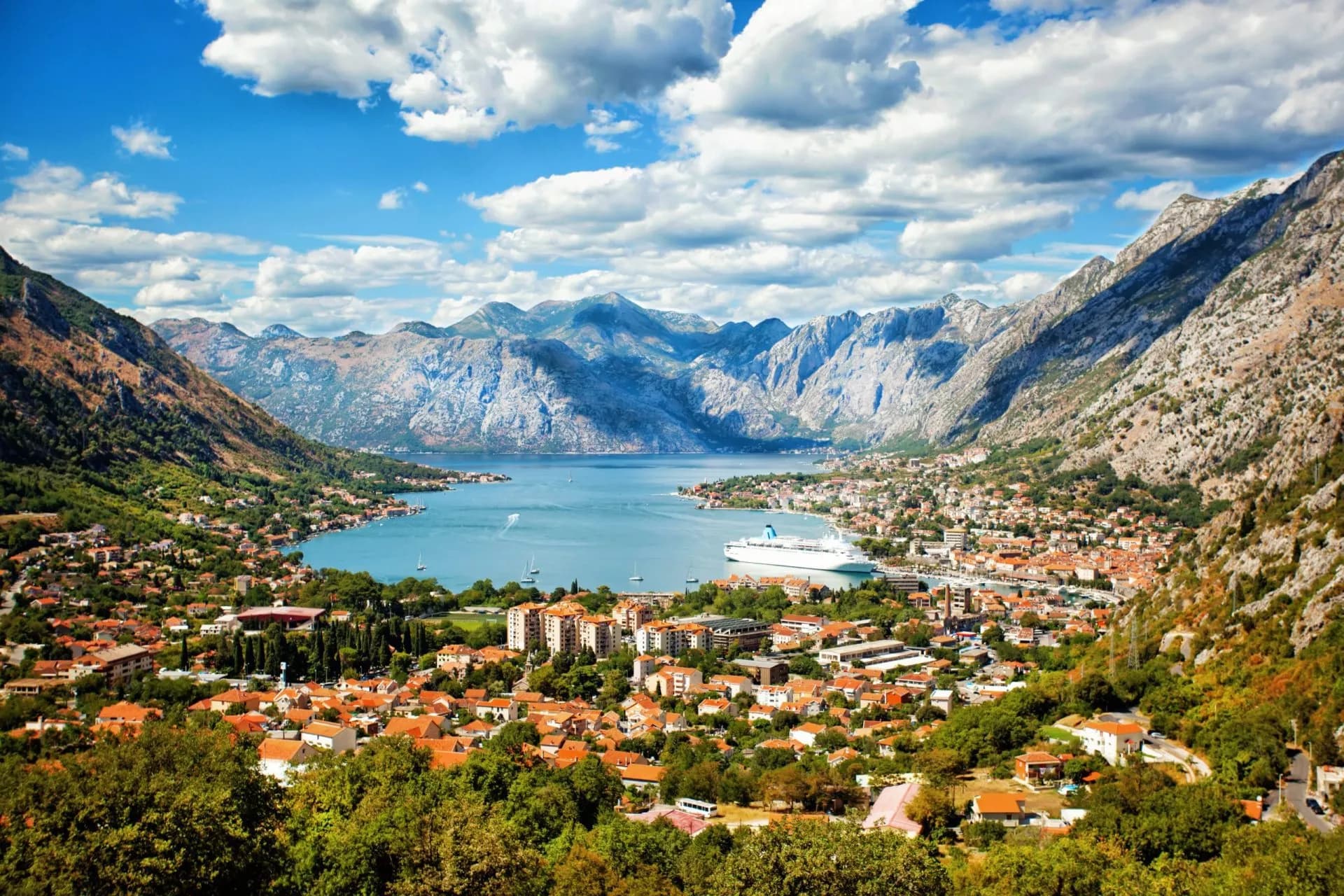 Coastal town nestled between steep mountains and a bay with a cruise ship in Montenegro.