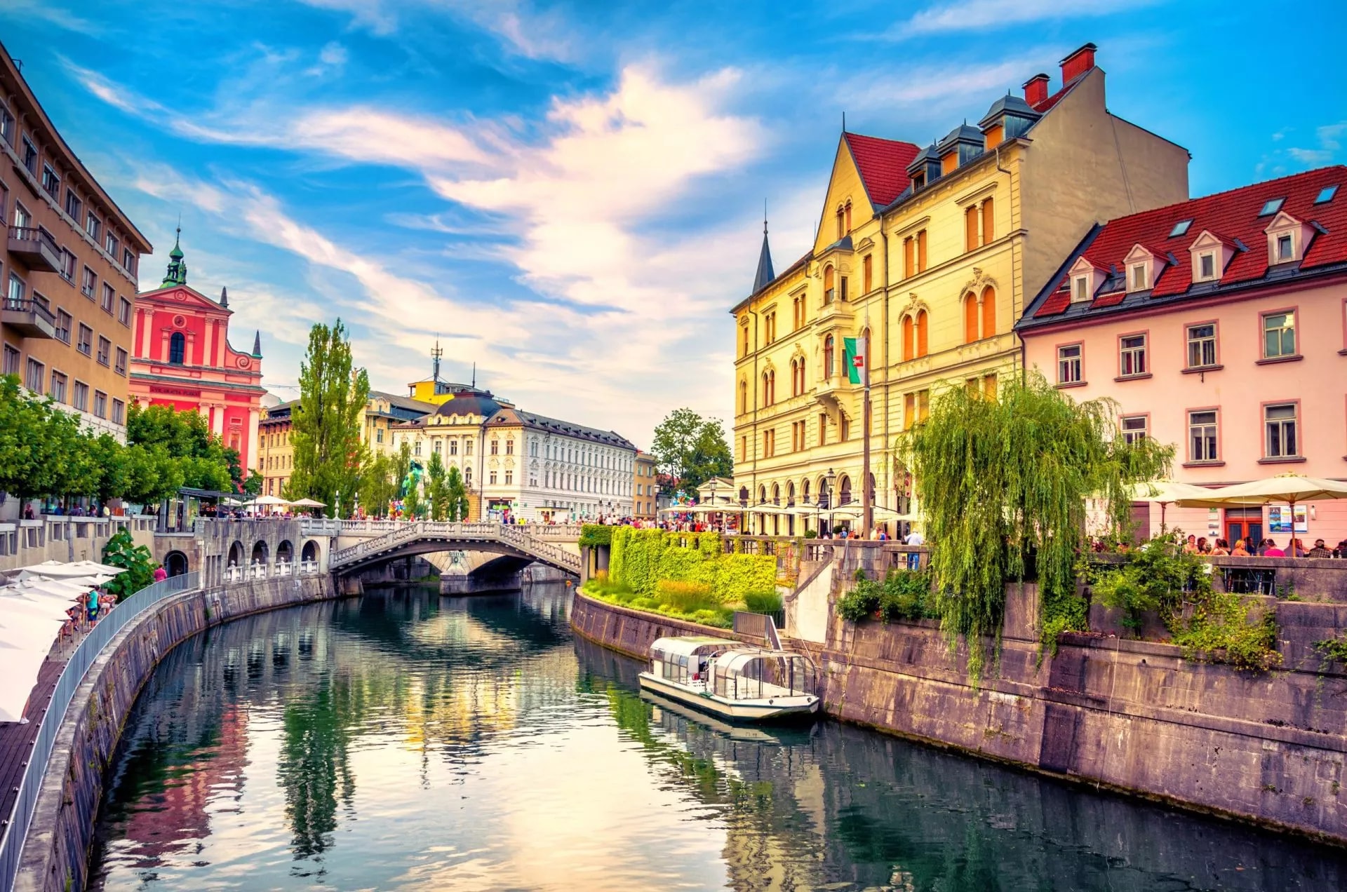 Cityscape view on Ljubljanica river canal in Ljubljana Old Town with tour boat and bridge.