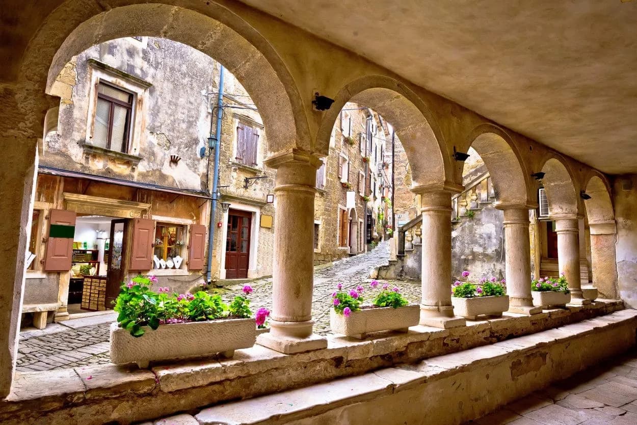Stone arcade with flower boxes overlooking a steep, cobblestone street in Grožnjan.