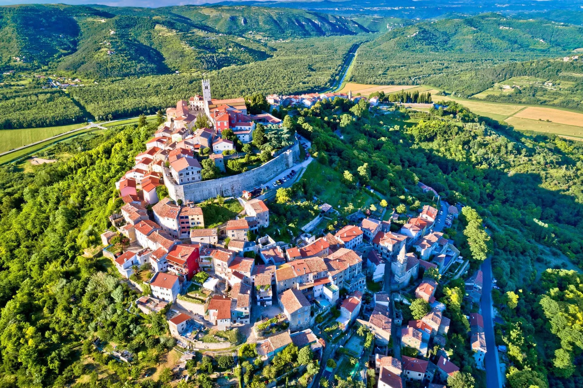 Aerial view of Motovun, a hilltop town with red-roofed buildings surrounded by lush green hills in Croatia.