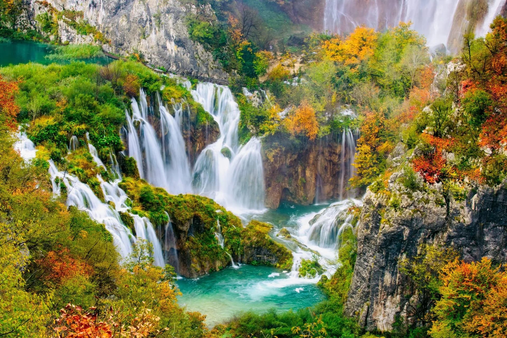 Waterfalls cascading over mossy rocks into turquoise pools in Plitvice National Park, Croatia in autumn.