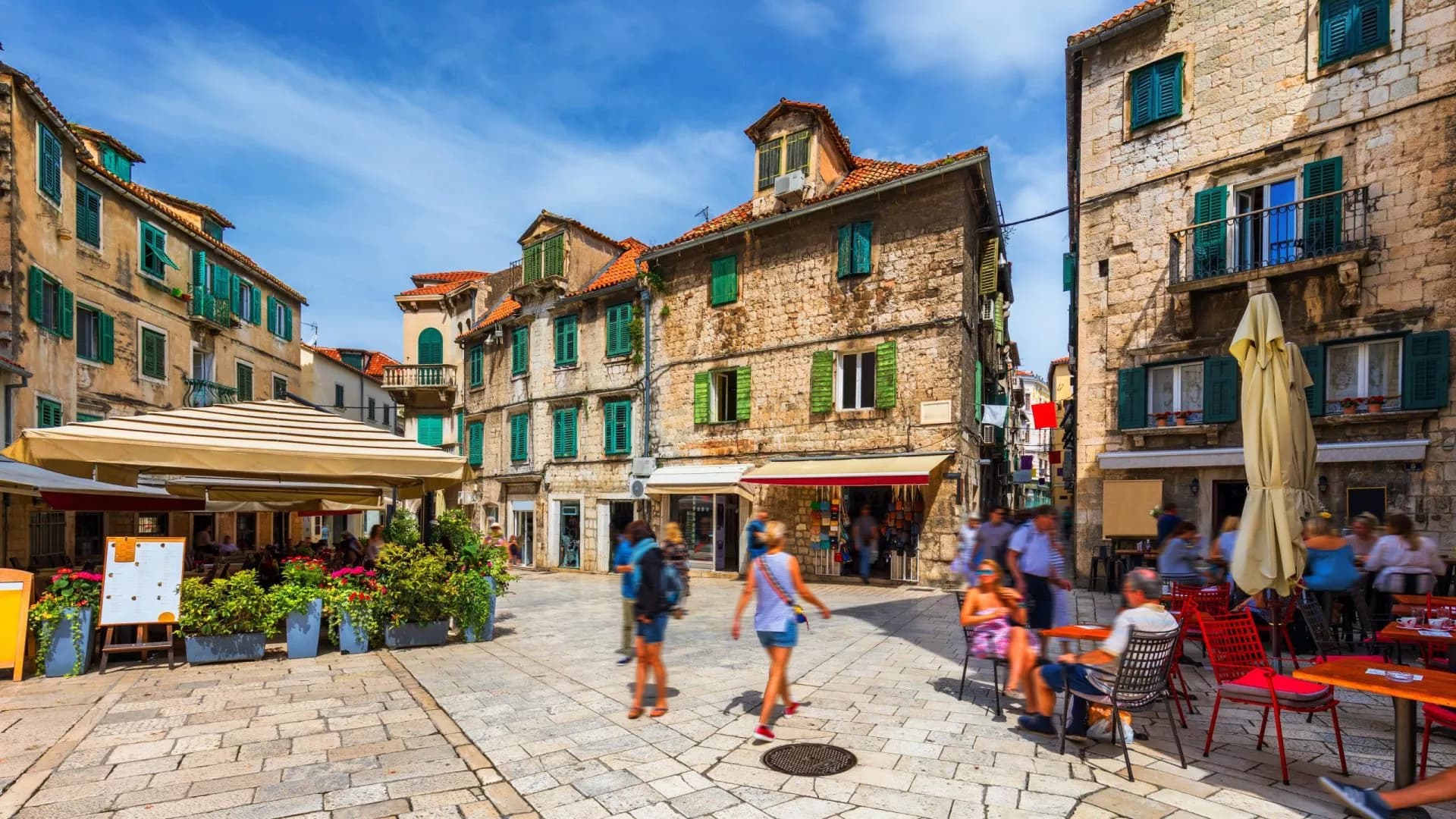 Old stone street in Split historic center, Croatia, with outdoor cafe seating and people.