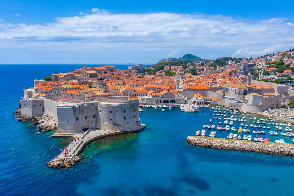 Dubrovnik, Croatia historic city walls and harbor filled with boats under a blue sky.