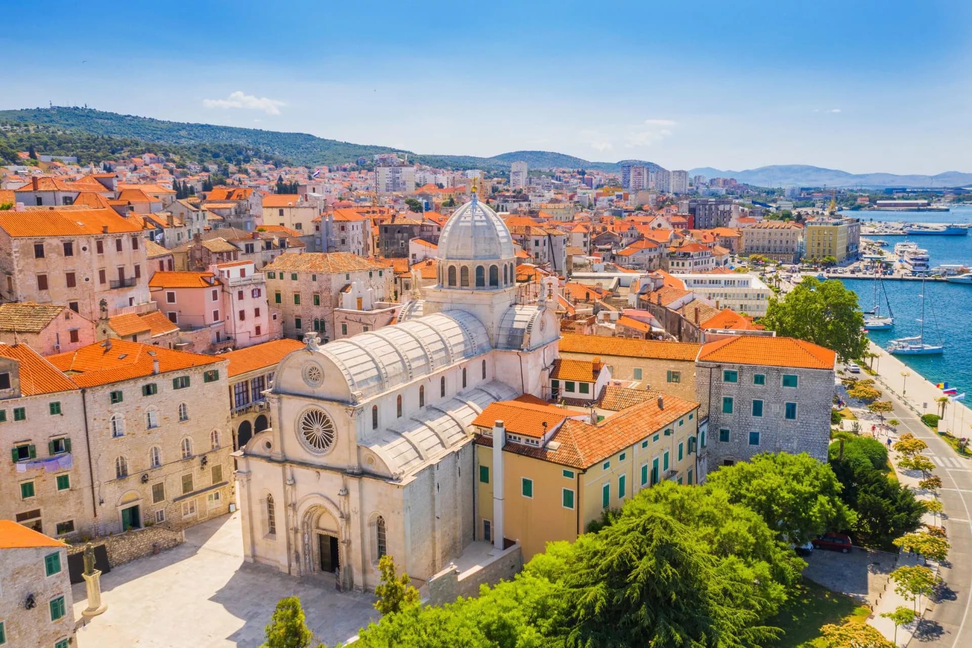 Panoramic view of Šibenik old town, St. James Cathedral, and harbor with boats under a blue sky.